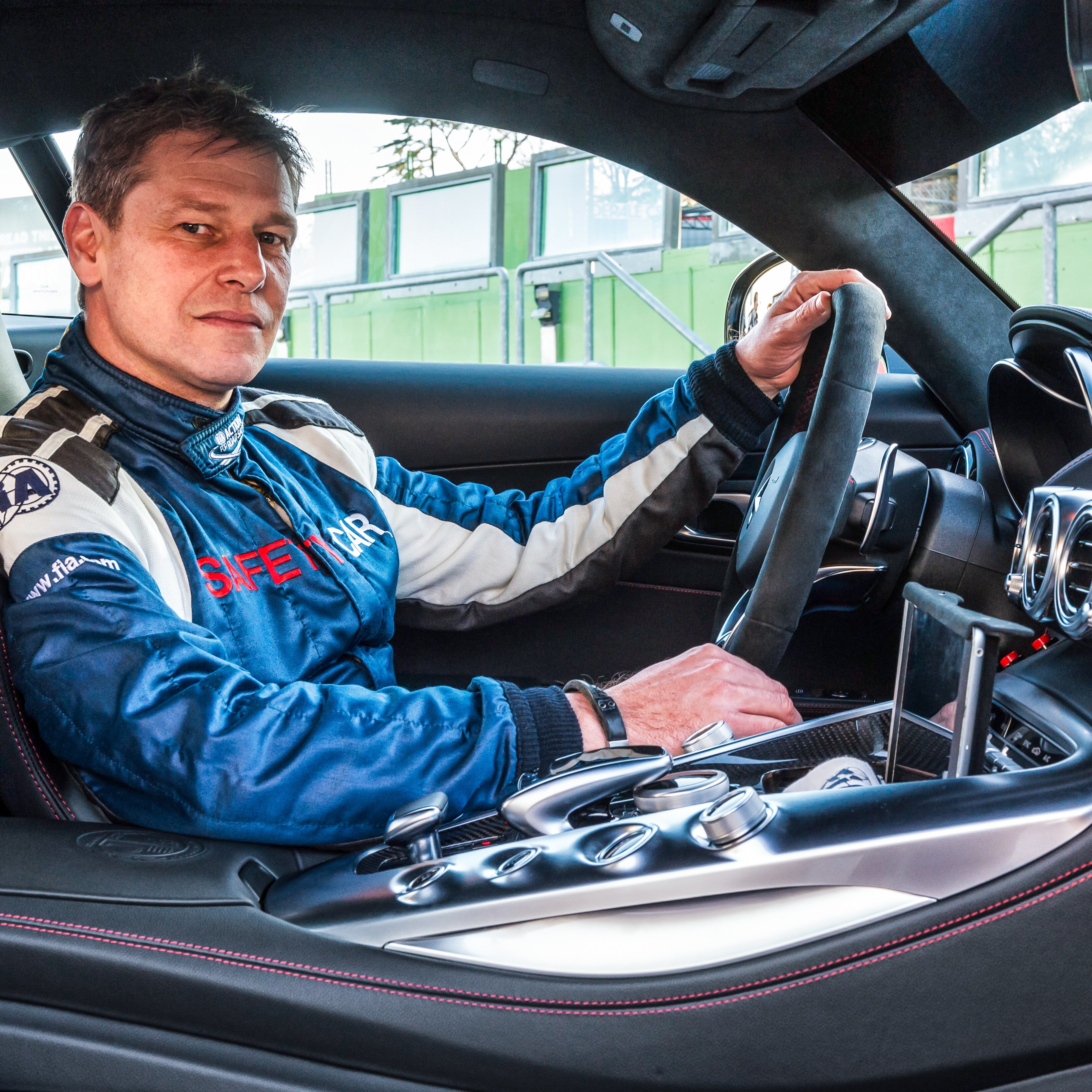 A man in black overalls stands next to a red Mercedes-AMG F1® Safety Car.