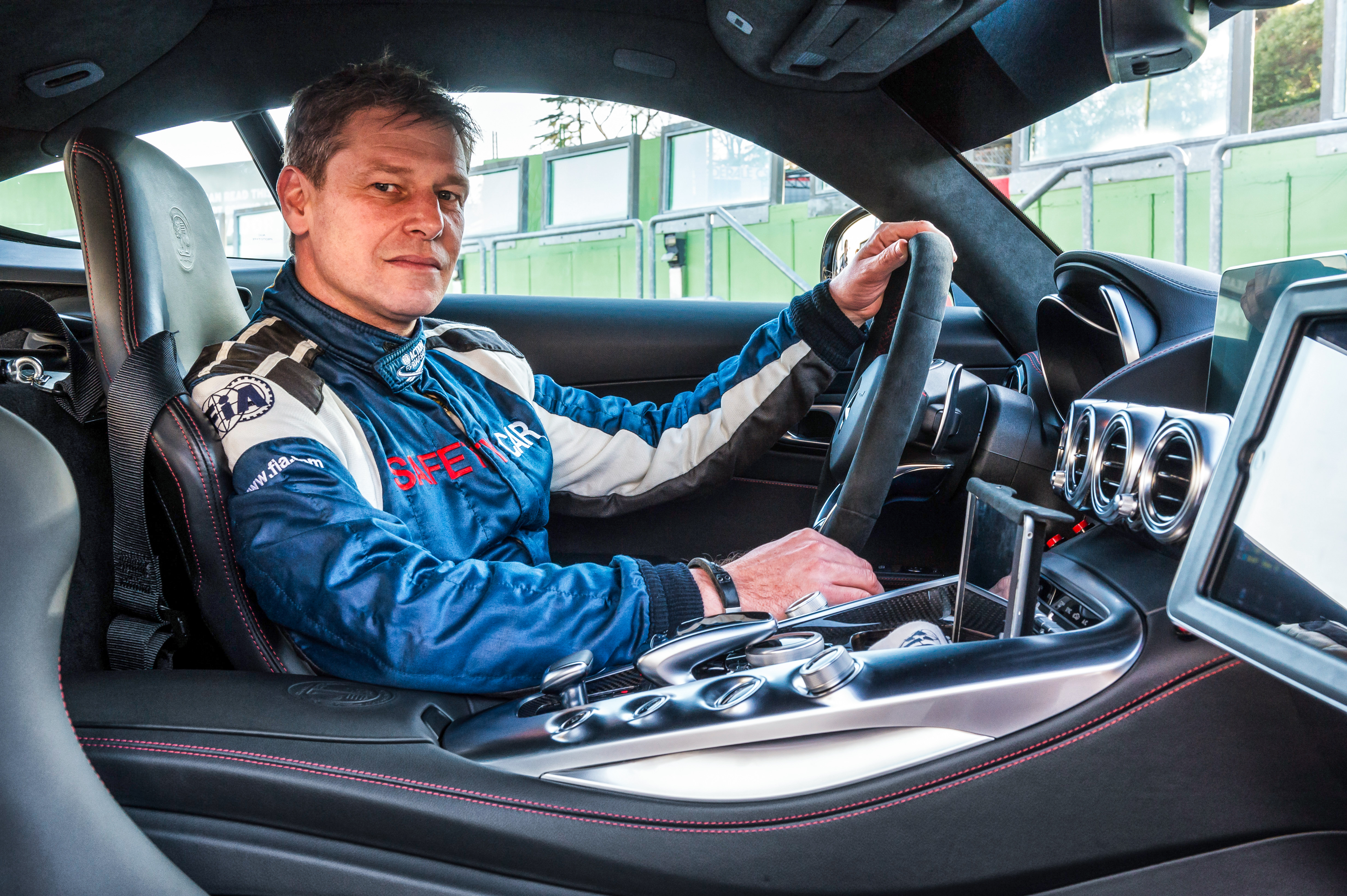A man in black overalls stands next to a red Mercedes-AMG F1® Safety Car. A man in black overalls stands next to a red Mercedes-AMG F1® Safety Car.