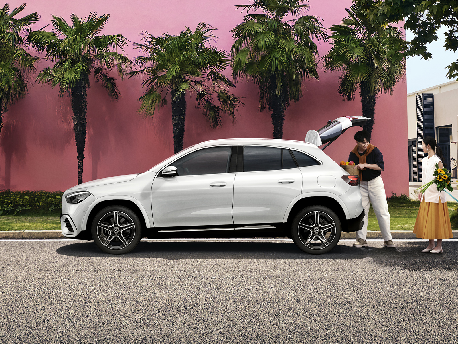 A man loads groceries into his white SUV, while a woman holding flowers stands nearby Couple loading groceries into a white GLA