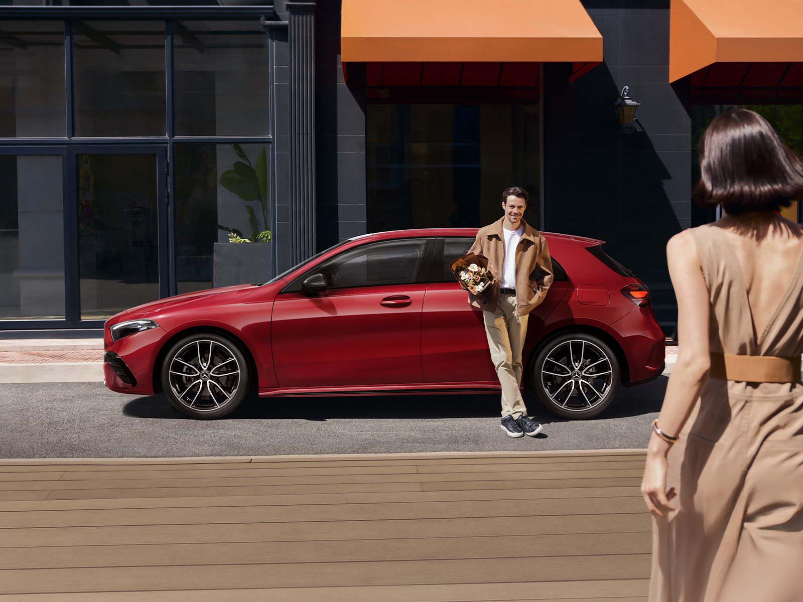 Man and his red A-Class Hatch Man leaning against his red car holding a bouquet of flowers