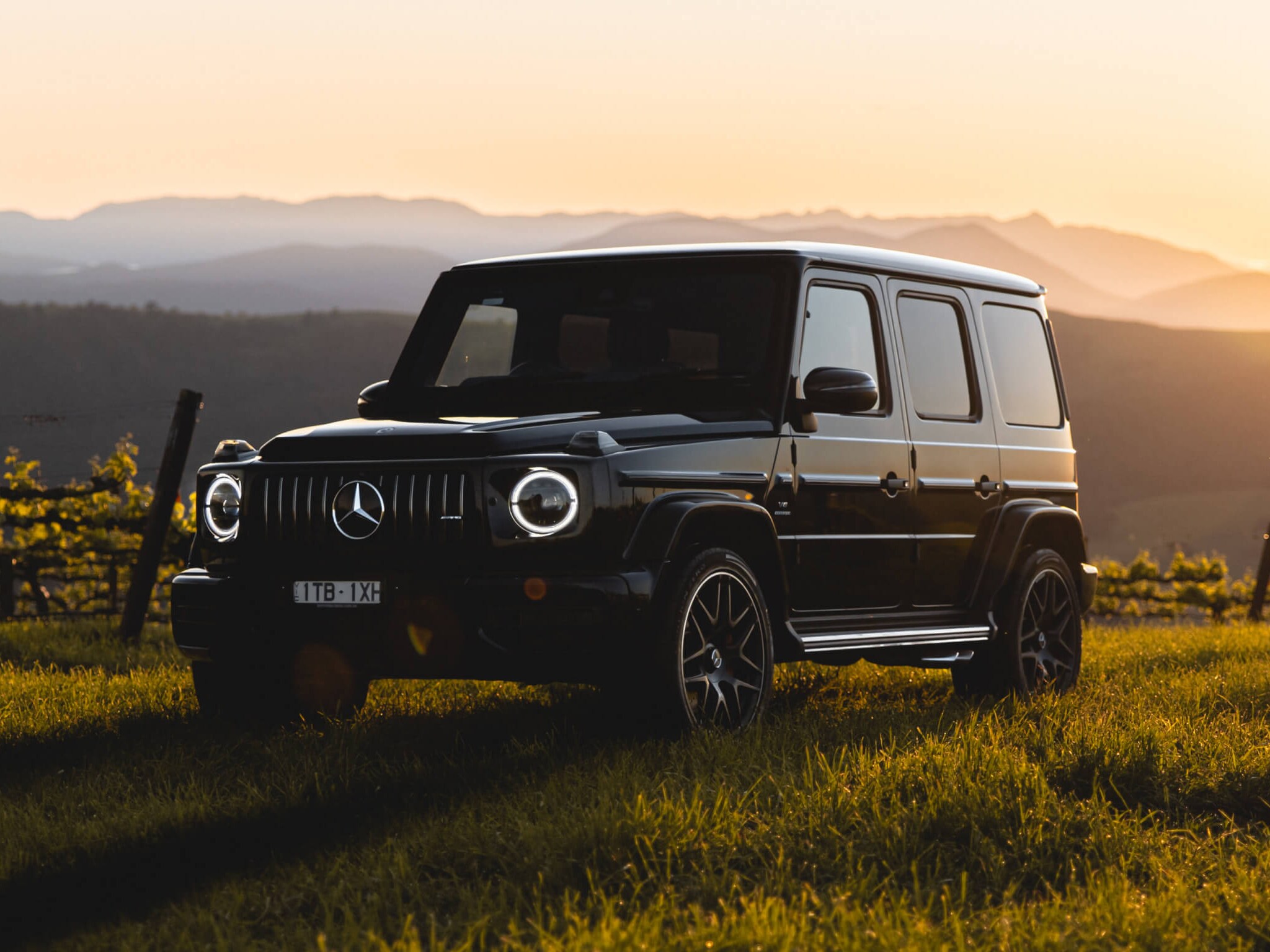 Mercedes-AMG G 63 driving across a grass field at twilight, surrounded by rolling hills.