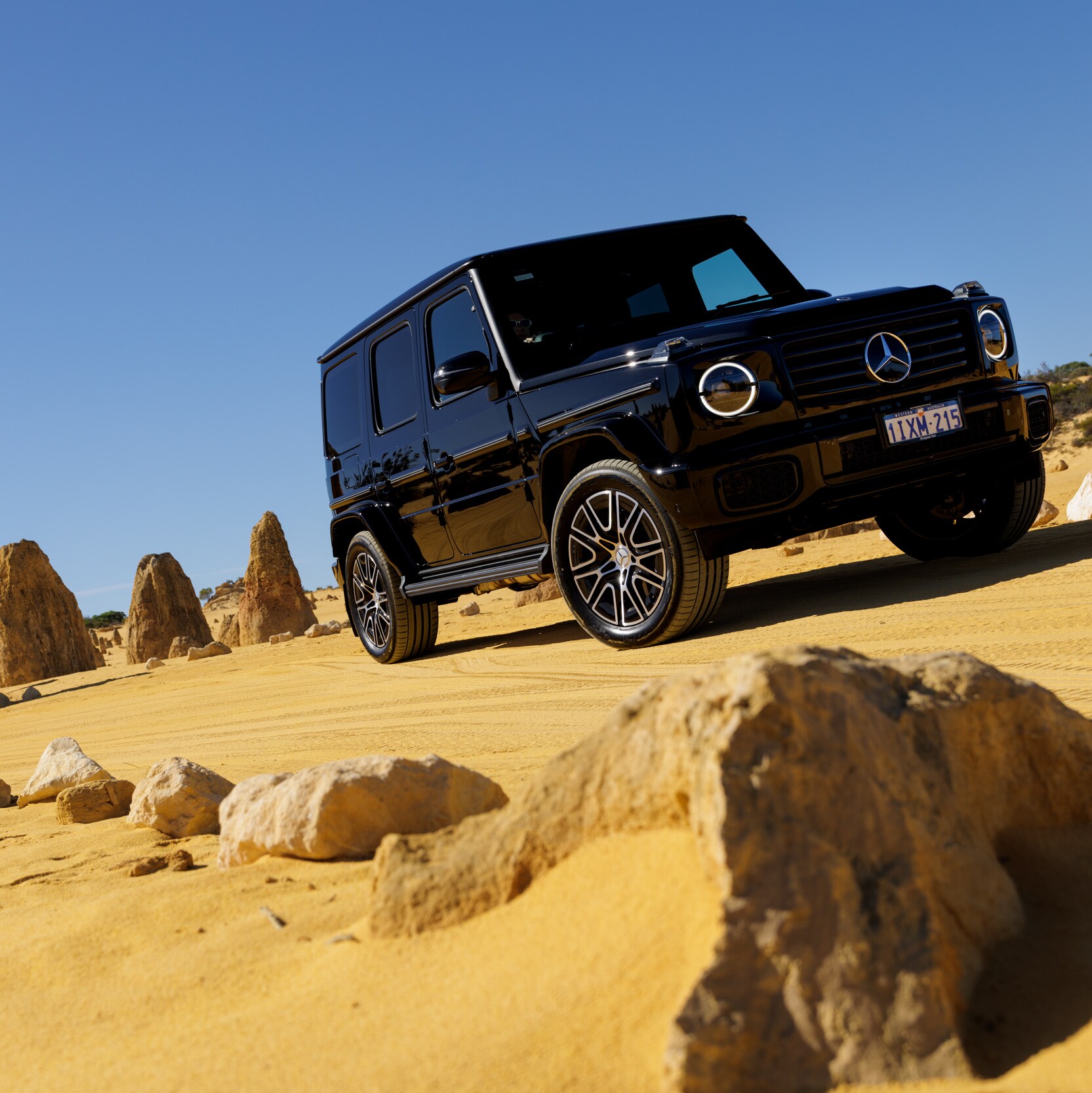 A black Mercedes-Benz G-Class driving through the yellow sands of The Pinnacles Desert in WA.