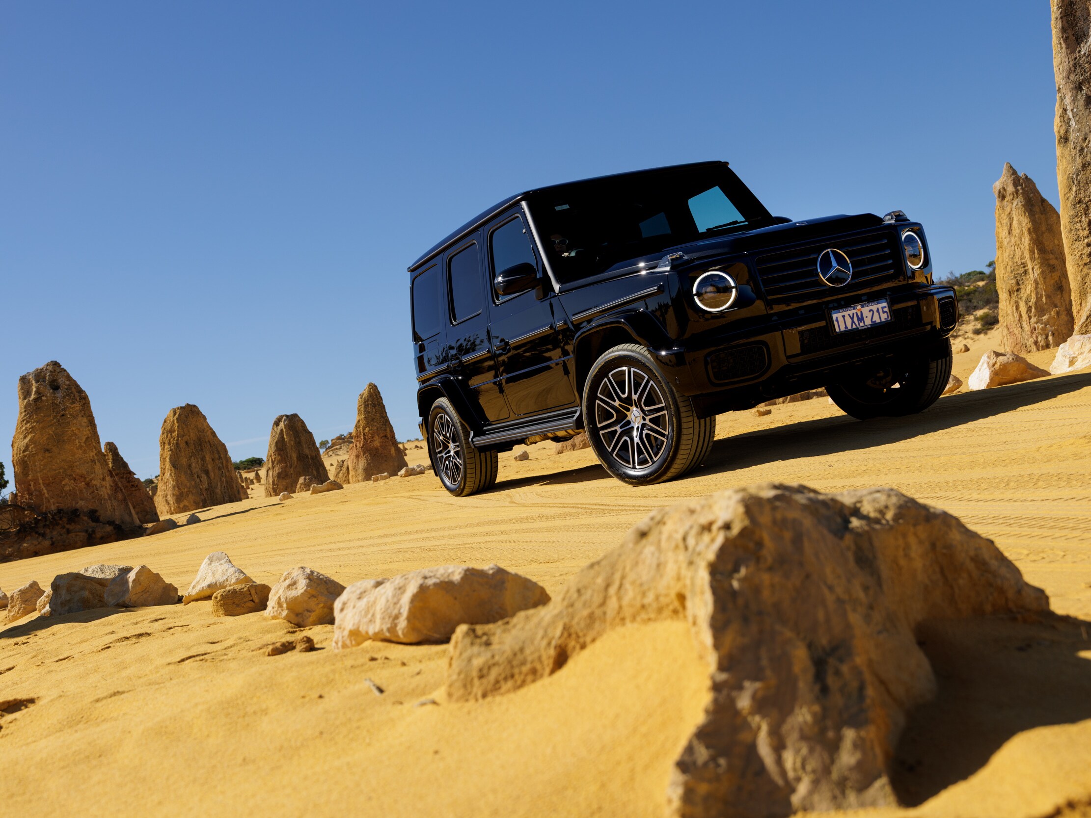 A black Mercedes-Benz G-Class driving through the yellow sands of The Pinnacles Desert in WA.