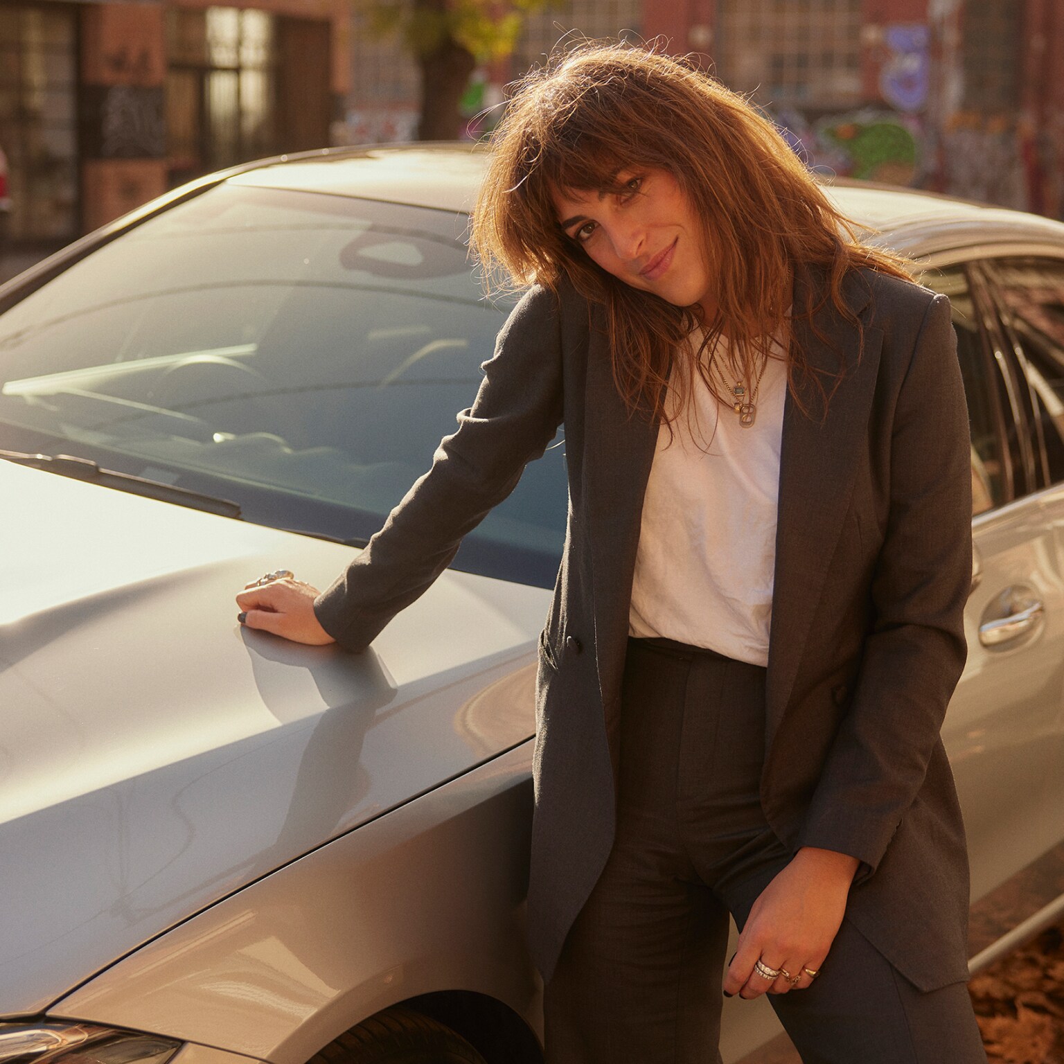 Emily Nolan leaning against the hood of a silver Mercedes-Benz C-Class C 200 Sedan and smiling.