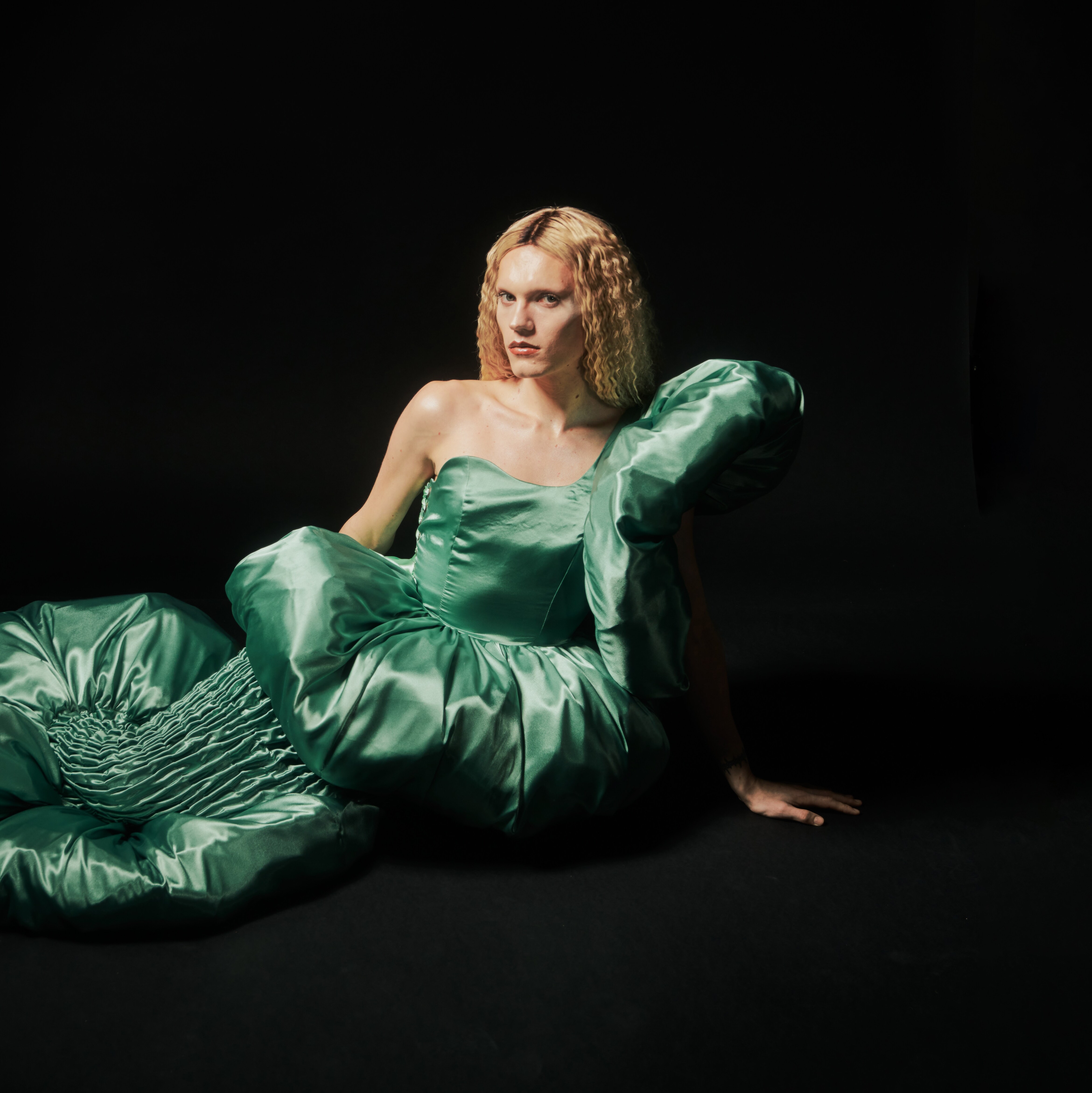 A person in a green dress designed by Jarrod Reid lying on their side. Image credit/photographer: Jess Brohier