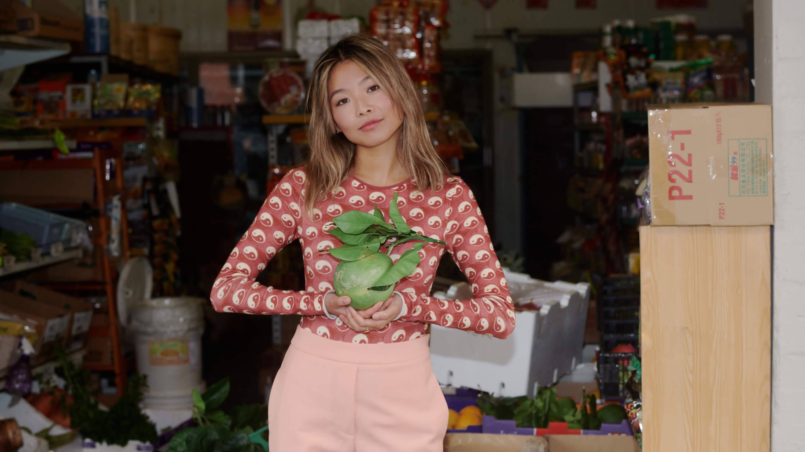Yan Yan Chan at an Asian grocery store Yan Yan Chan wears a red outfit and holds fruit at an Asian grocery store.