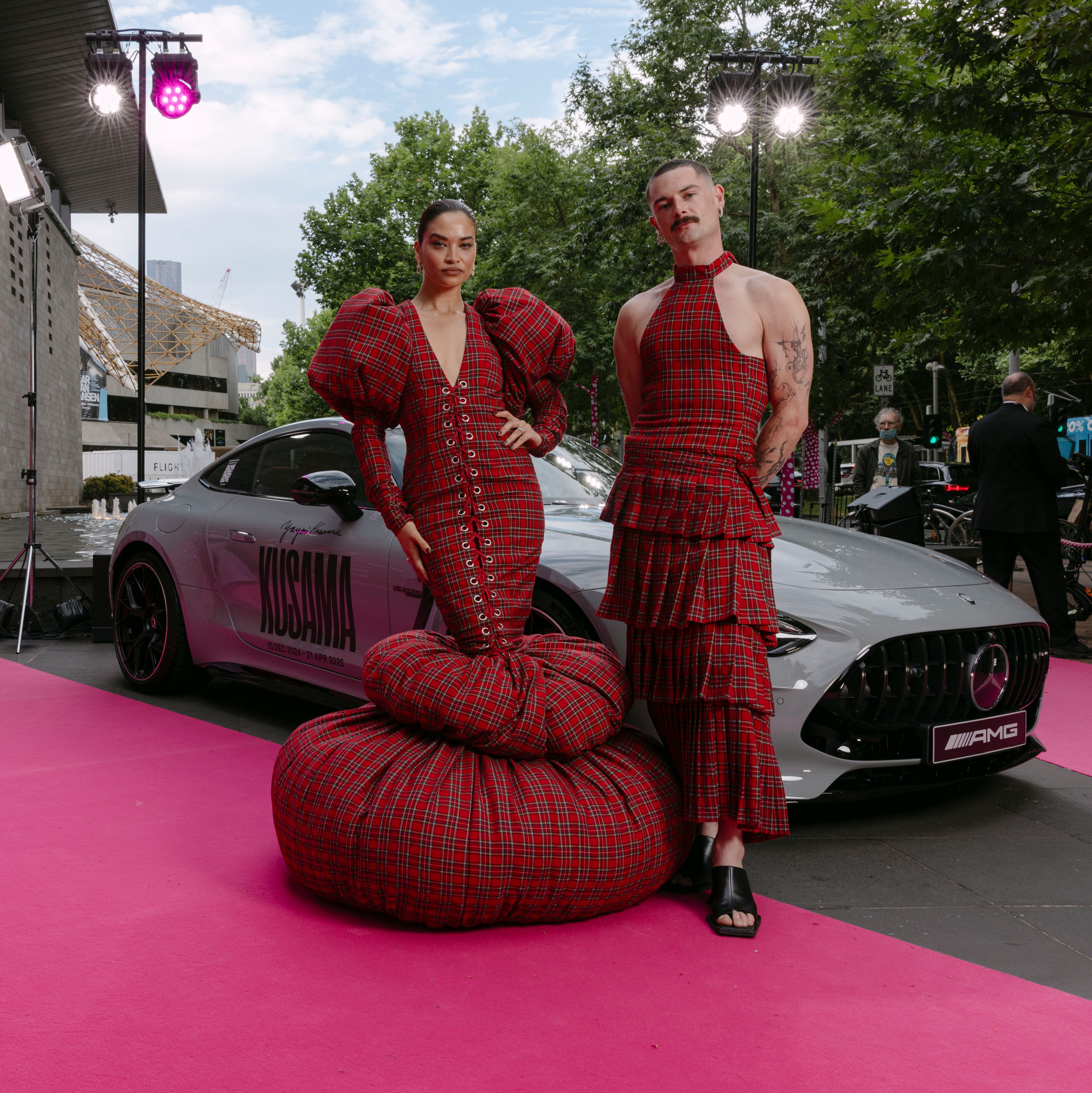 Model Shanina Sheik and fashion designer Jarrod Reid posing in tartan next an alpine grey Mercedes-AMG GT Coupe on the pink carpet outside the NGV