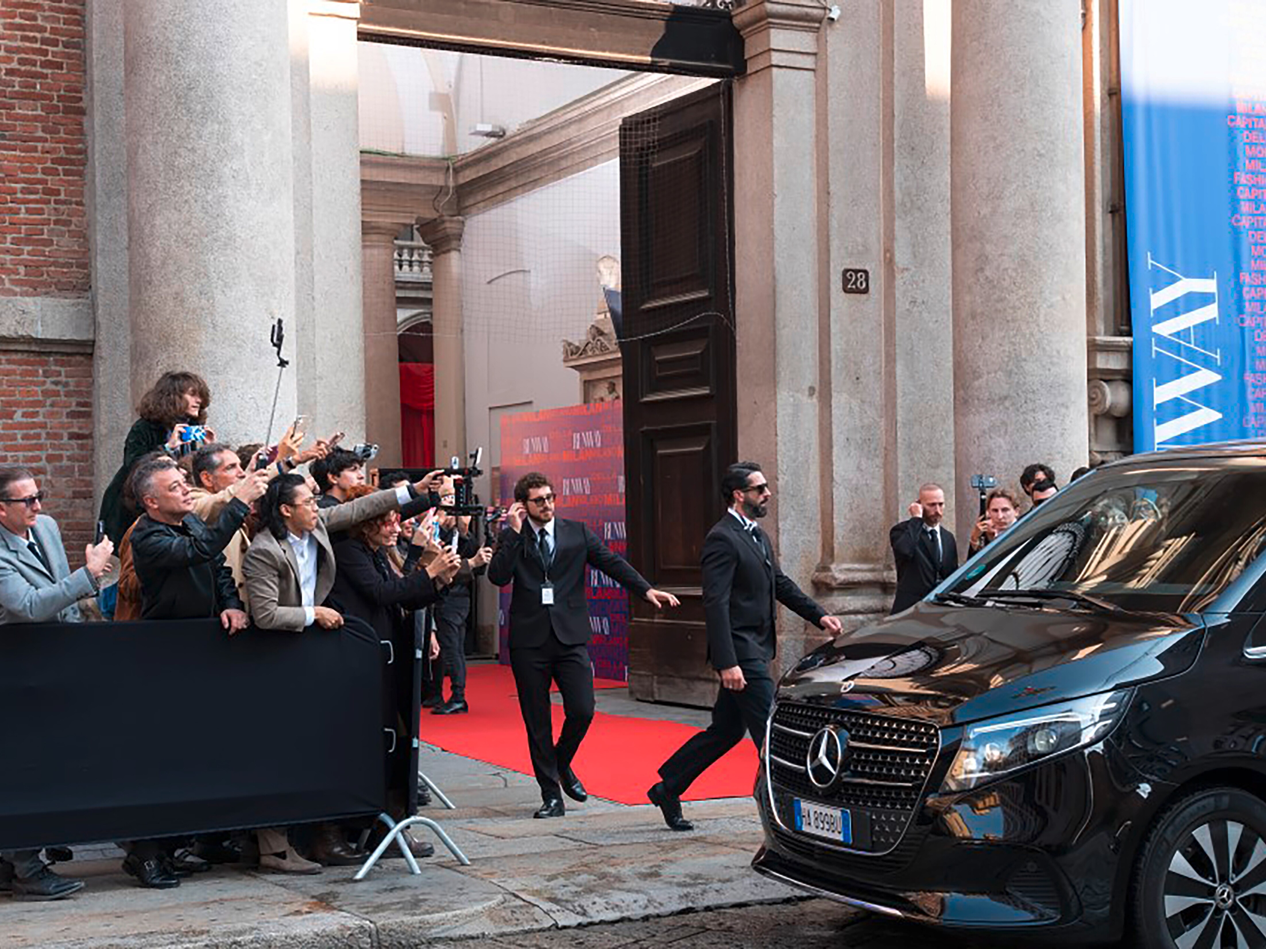 Paparazzi crowding by a car outside the entrance to a building