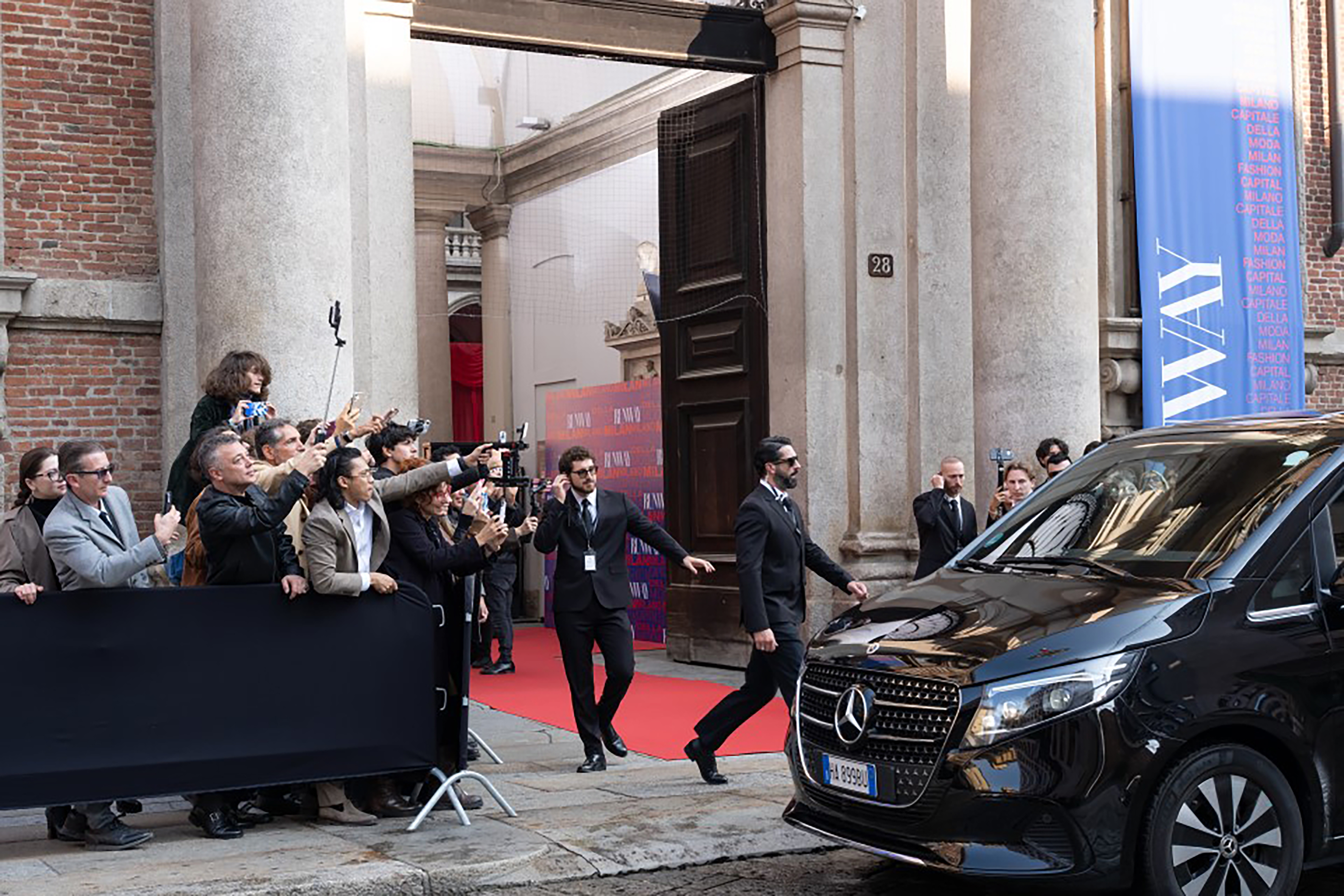 Paparazzi crowding by a car outside the entrance to a building Paparazzi crowding by a car outside the entrance to a building