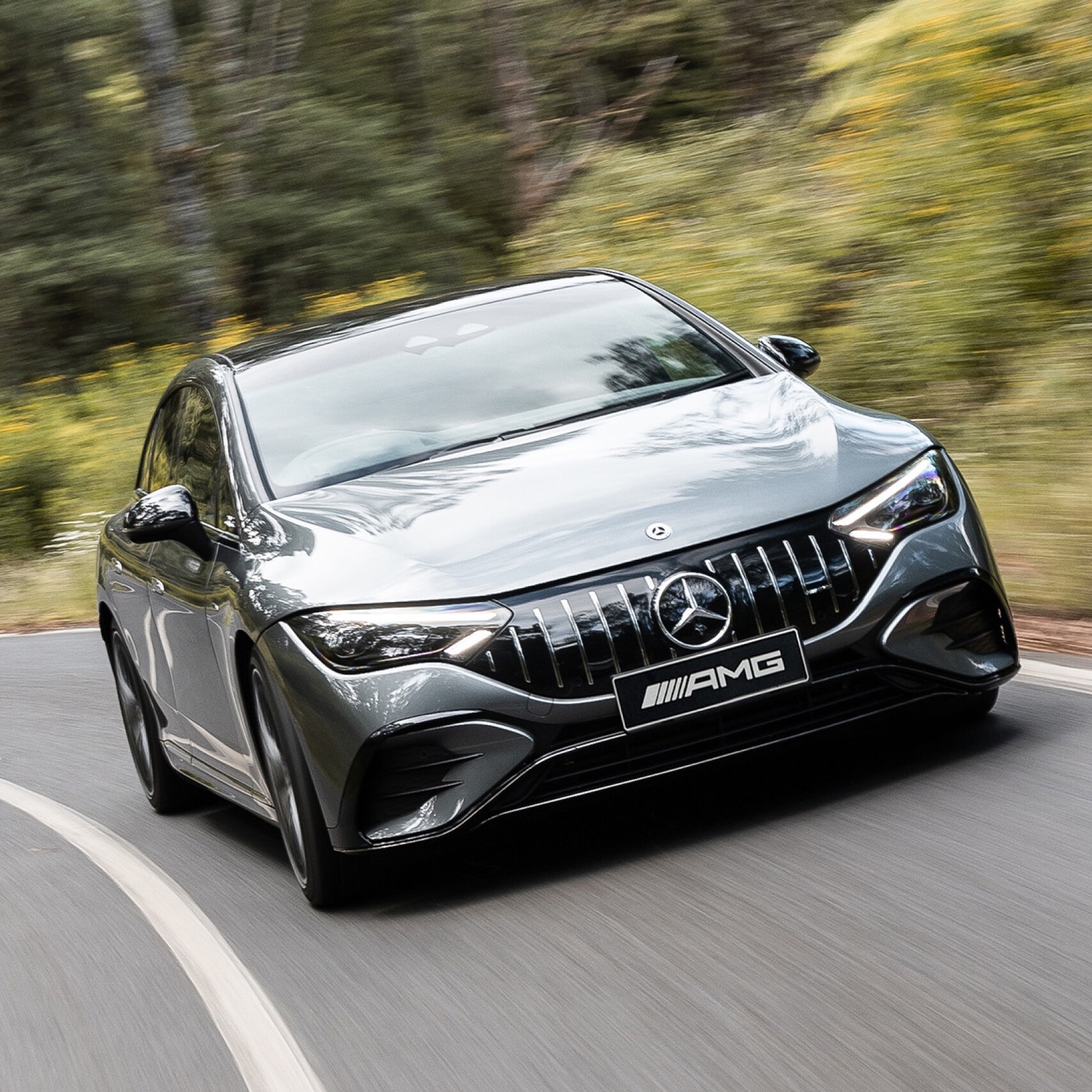 A grey all-electric Mercedes-AMG EQE 53 driving down a winding country road.