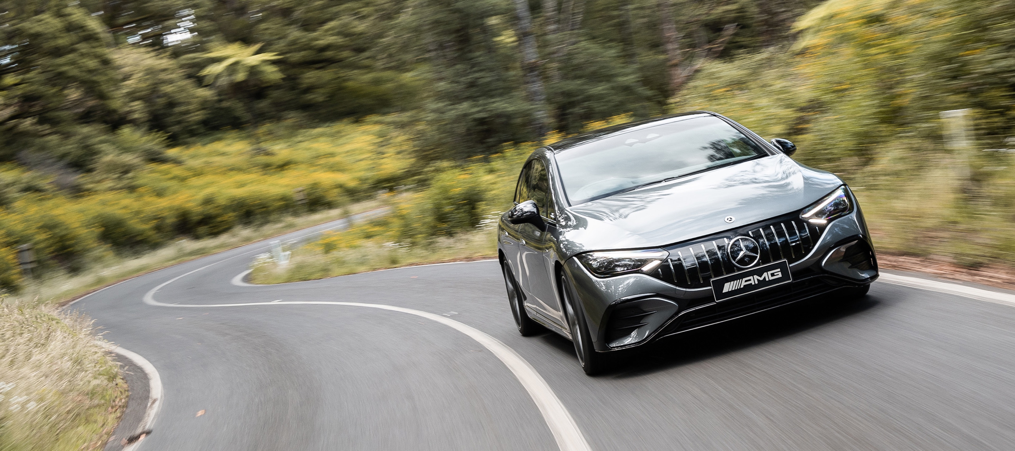 The all-electric Mercedes-AMG EQE 53 A grey all-electric Mercedes-AMG EQE 53 driving down a winding country road.