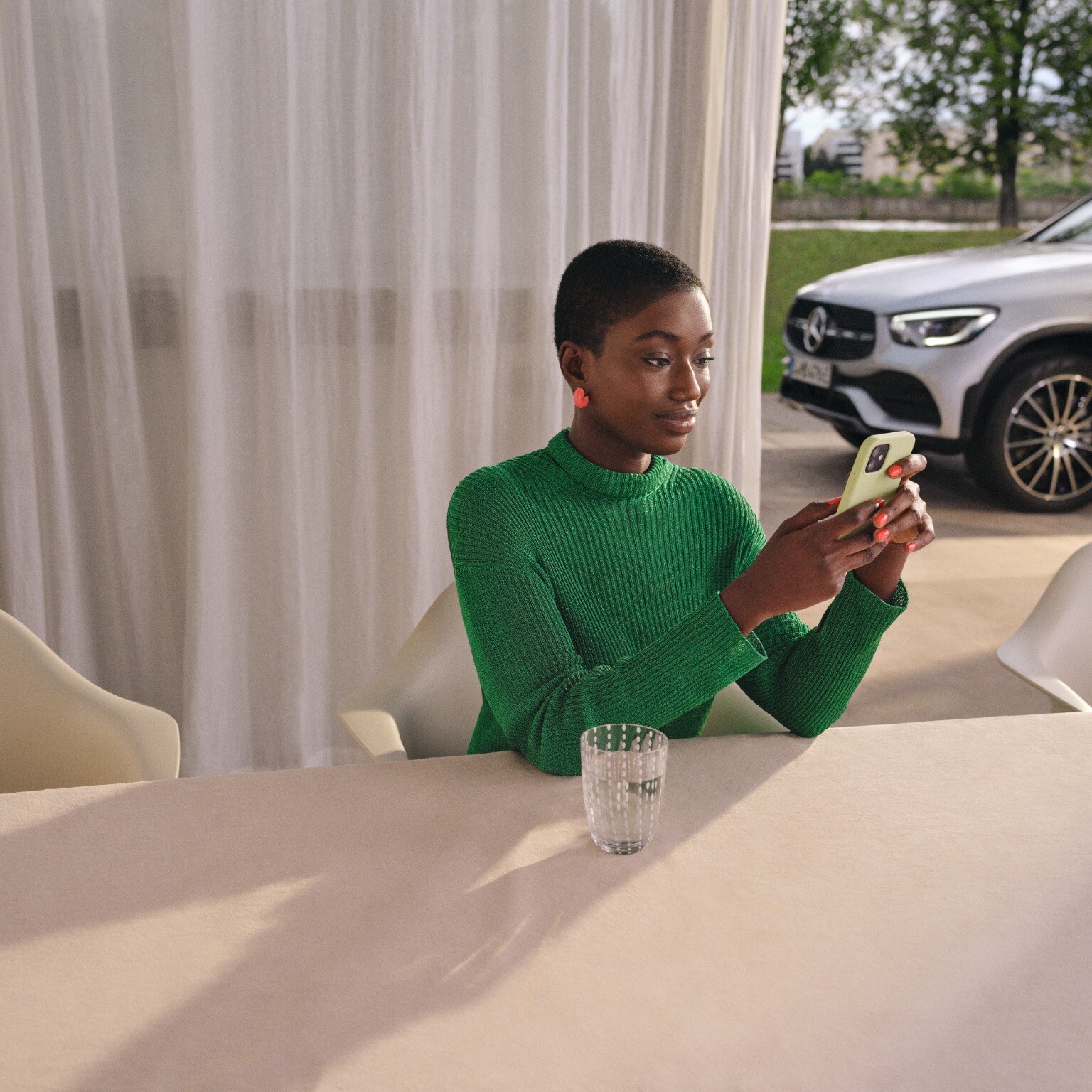 A woman sitting at a table on her phone with a Mercedes-Benz vehicle in the background.