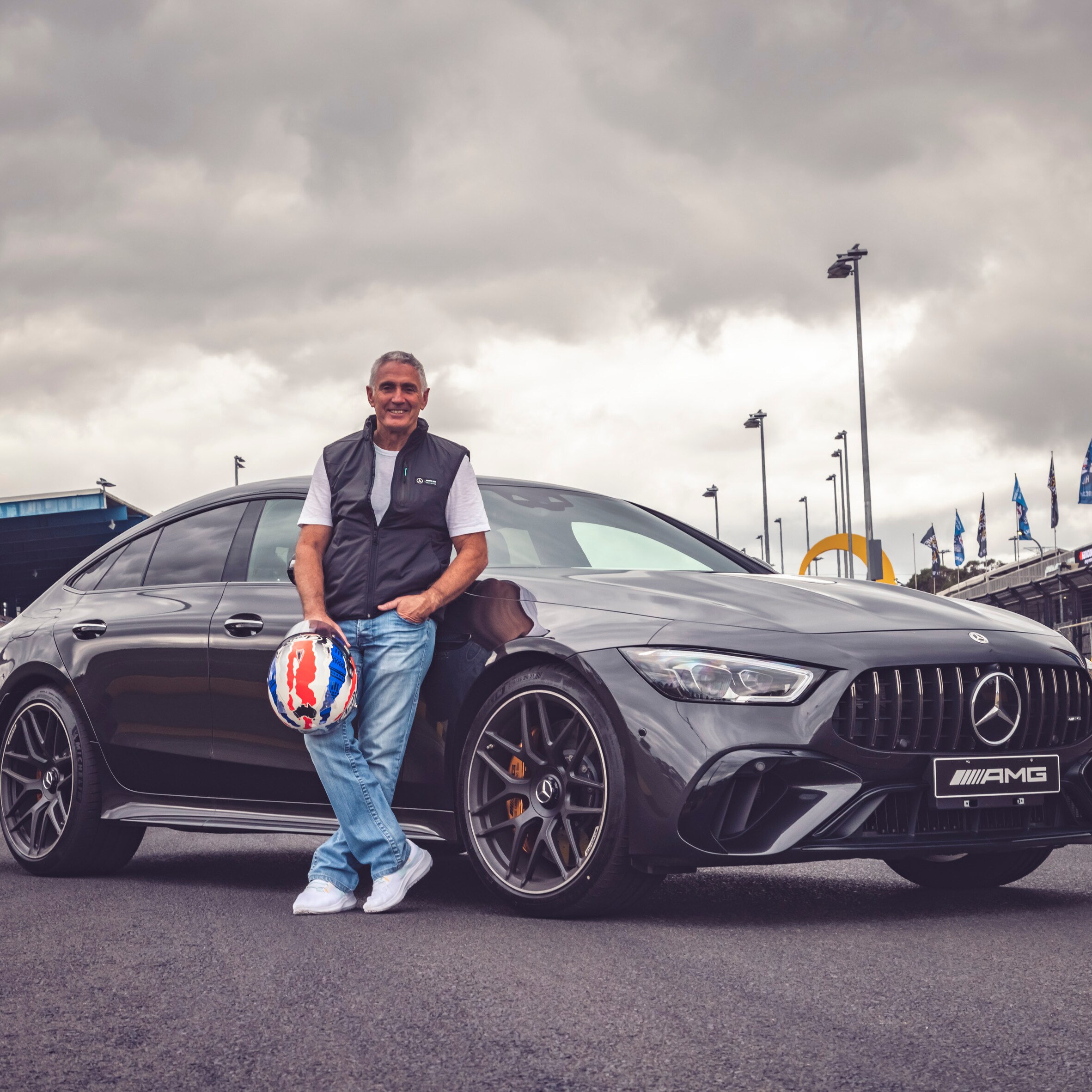 Mick Doohan holding motorcycle helmet standing in front of Mercedes-AMG