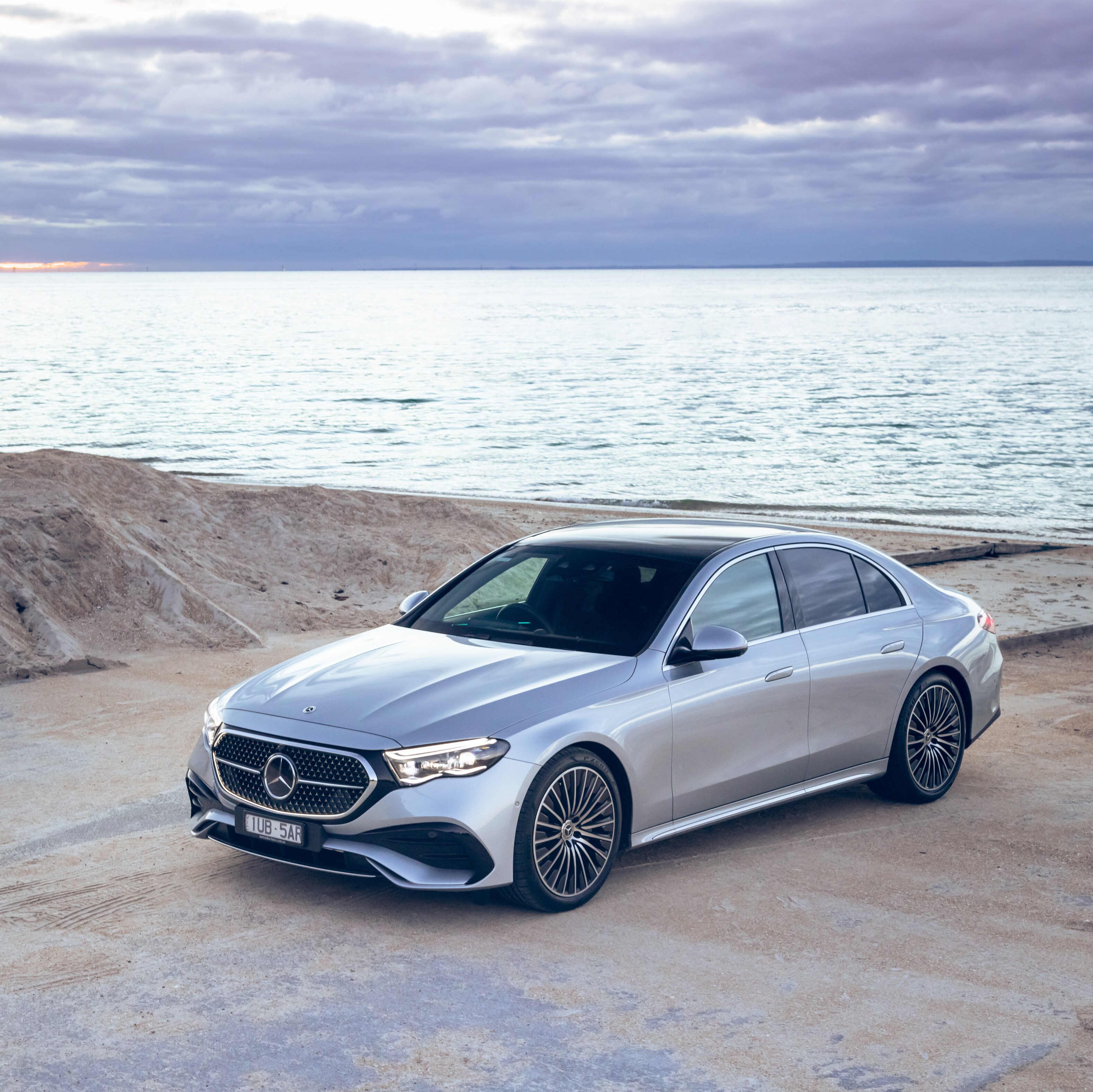 A silver Mercedes-Benz E-Class parked by a beach