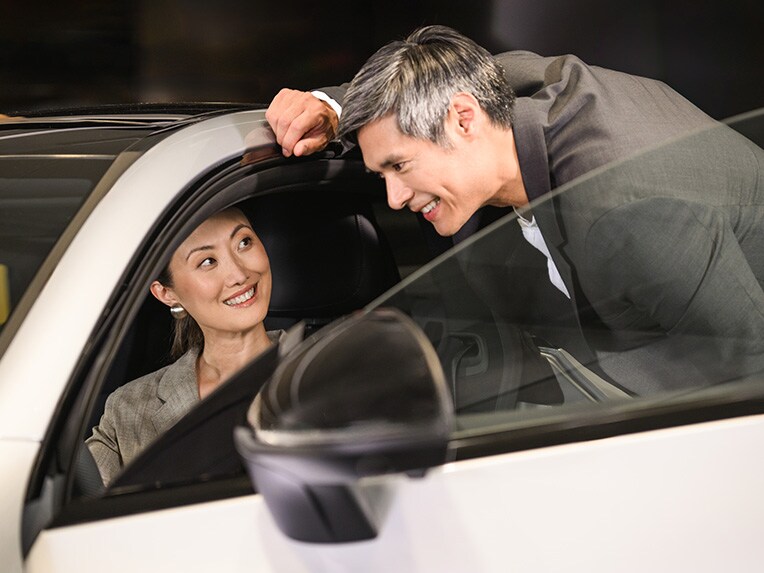 A person sitting in the drivers seat of a Mercedes-Benz vehicle with someone looking inside the passenger side door open.