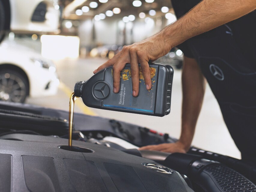 Close‑up of engine bay with Mercedes‑Benz genuine engine oil being poured.