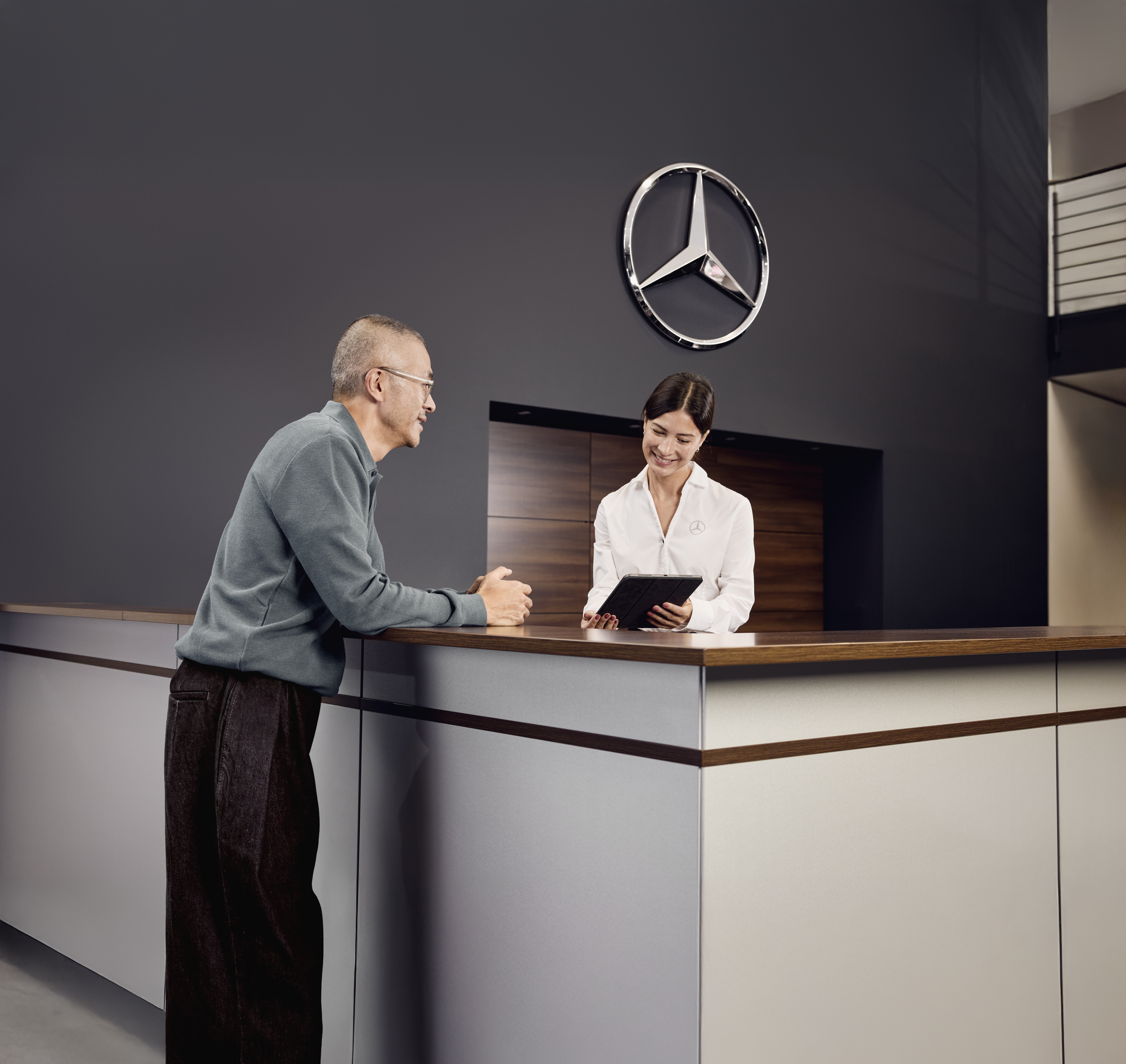 Mercedes‑Benz Genuine Parts Consultation Service reception area at a Mercedes‑Benz dealership where a customer discusses vehicle service details with a service advisor at the front desk.