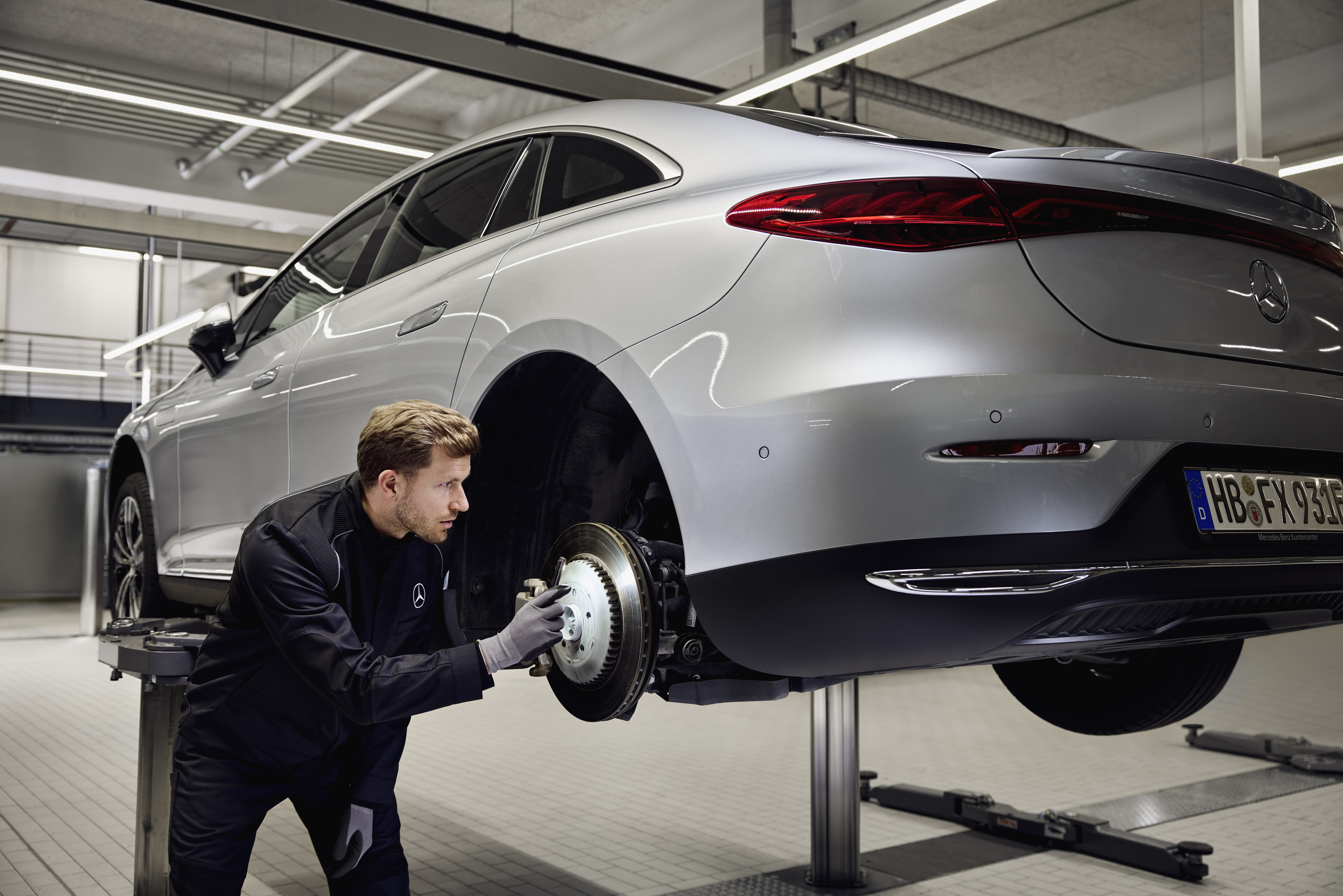 Mercedes‑Benz Genuine Brake Replacement Mercedes‑Benz vehicle raised on a lift with a technician inspecting the rear brake system for a replacement of genuine parts service.