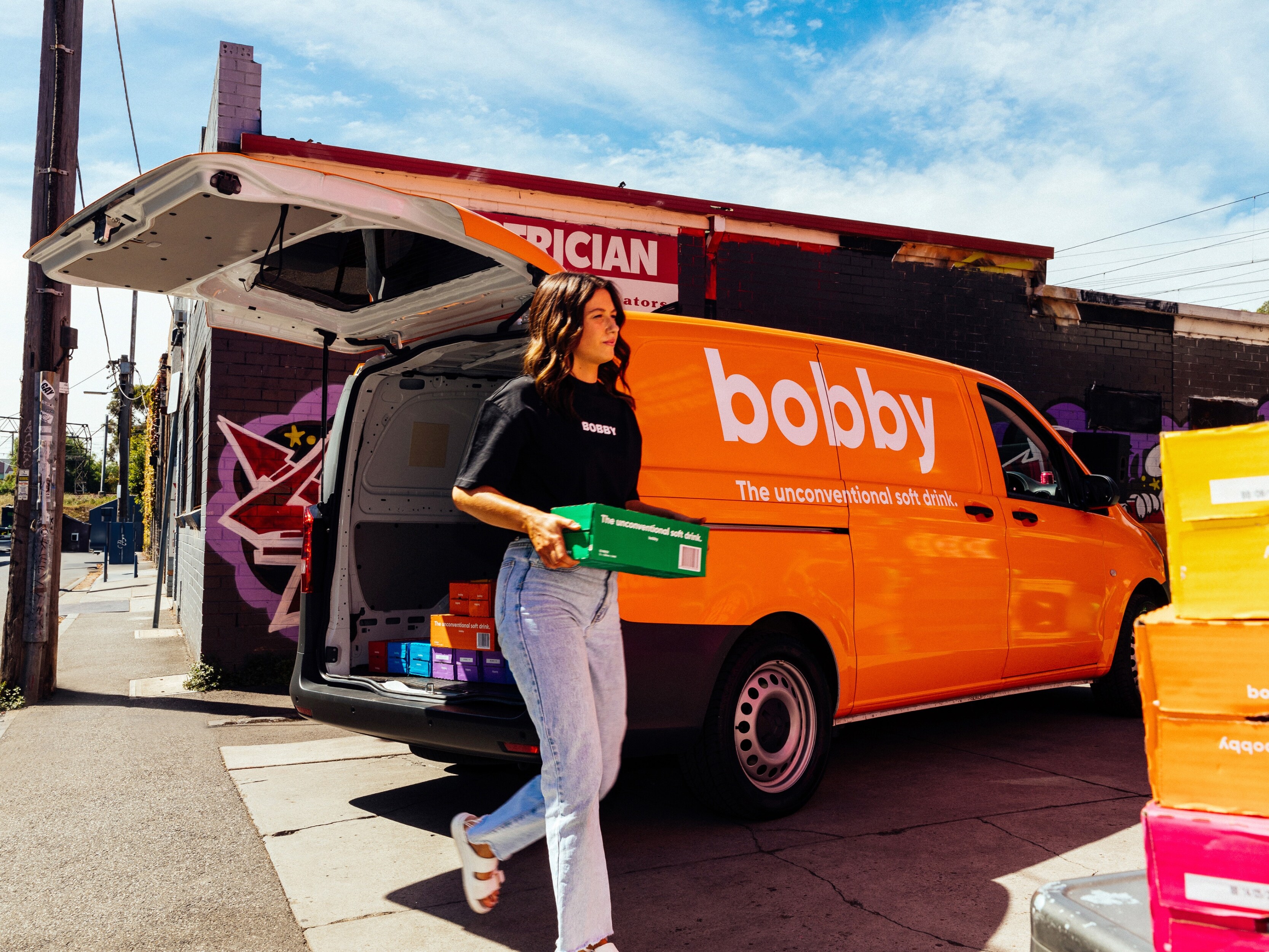 A person carrying  a box of soft drink from an orange van.