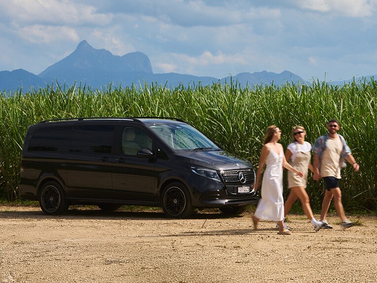 Three people walk past V-Class, against a mountain range