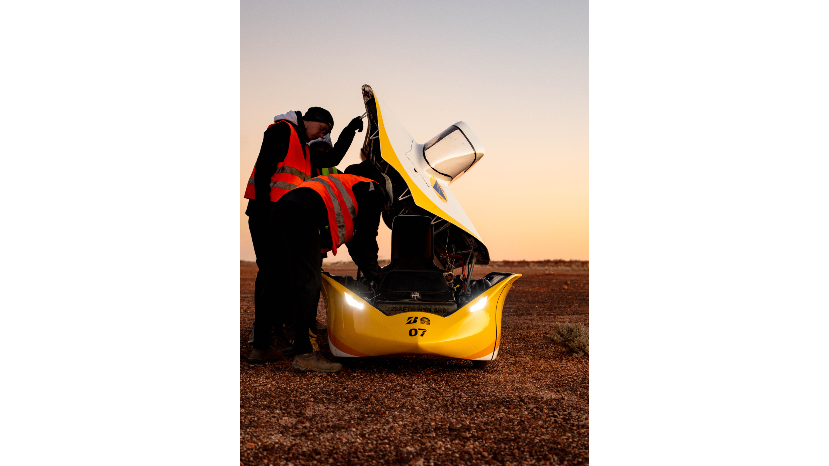 Team Sonnenwagen Yellow-and-white solar race car beside a black Mercedes-Benz V-Class on a desert road.