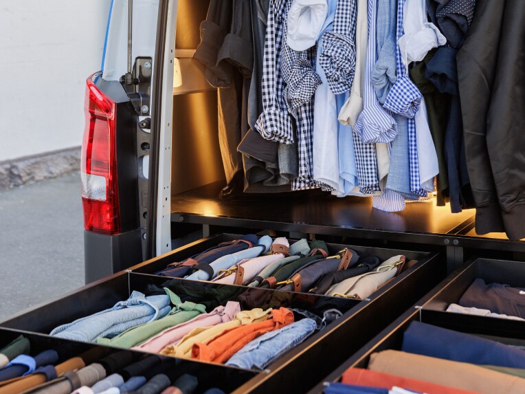 A van with clothes hung up in back and drawers open full of apparel.