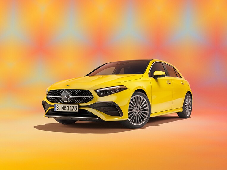 The image shows a slanted front view of a Mercedes-Benz A-Class in a yellow studio.