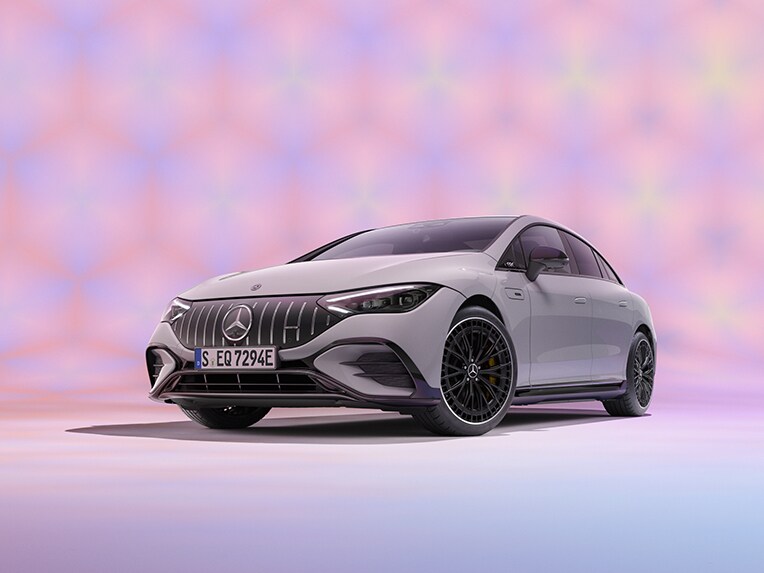 The image shows the angled front view of a Mercedes-Benz EQE in a pink studio.