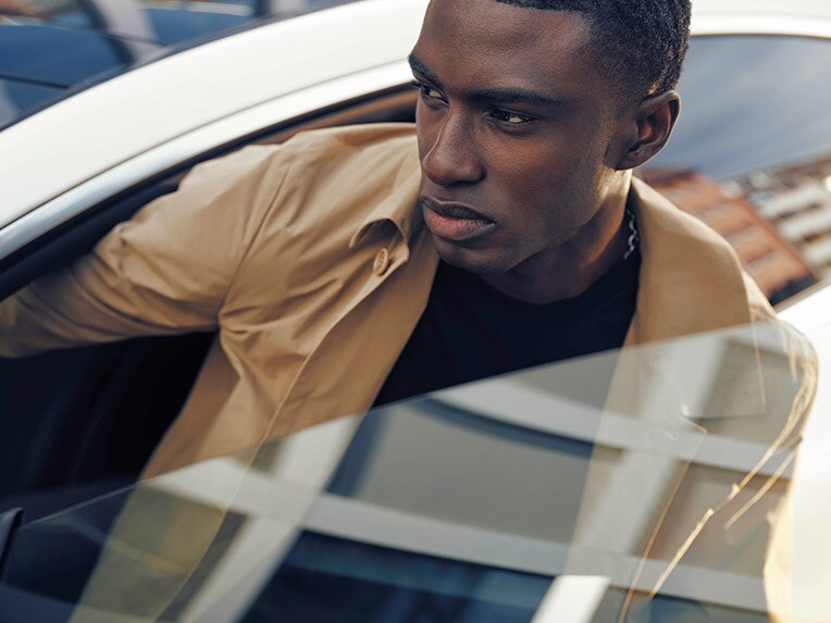 A person sitting in the drivers seat of a Mercedes-Benz vehicle with someone looking inside the passenger side door open.