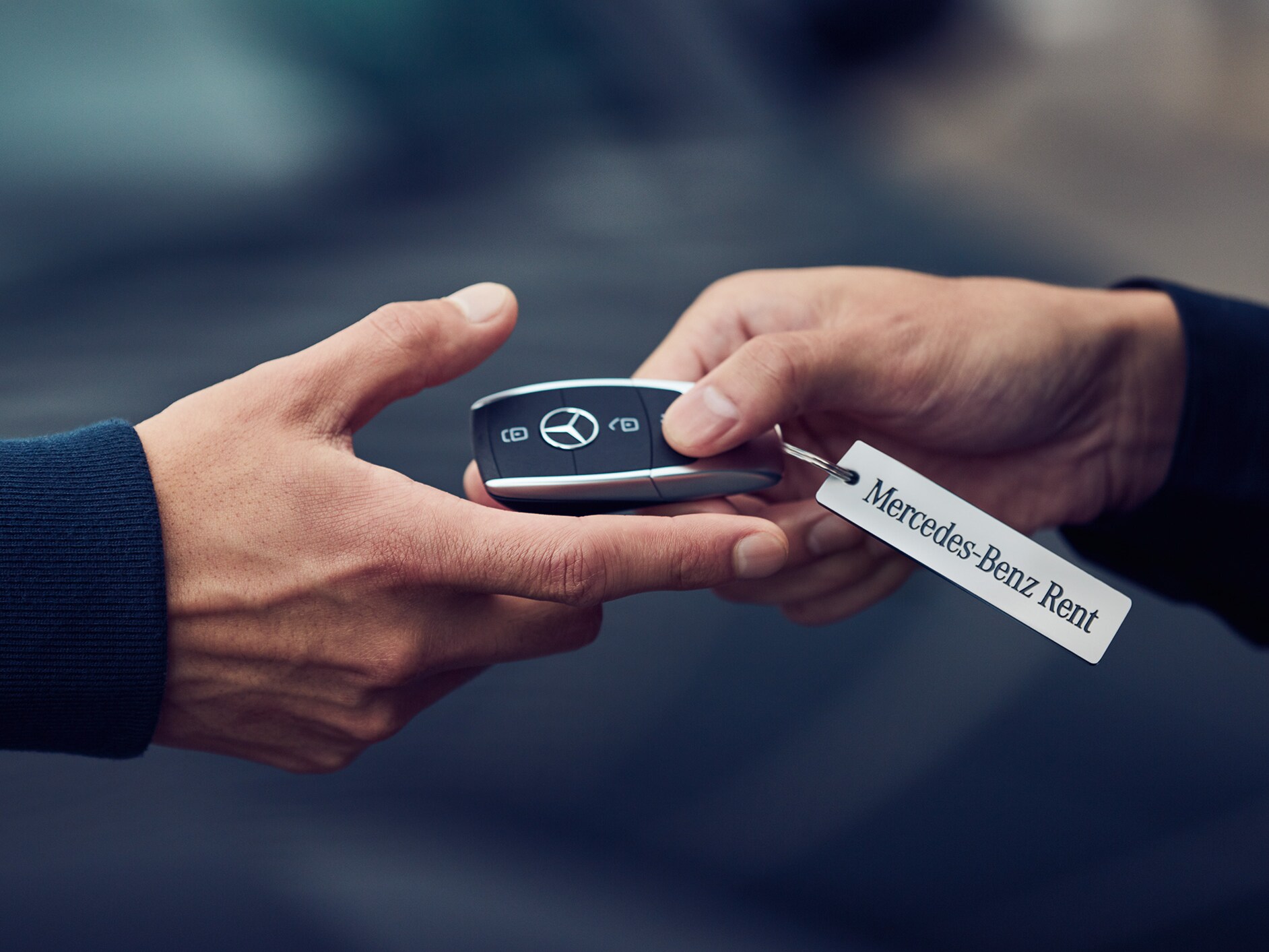 Two hands passing each other a key from Mercedes-Benz.