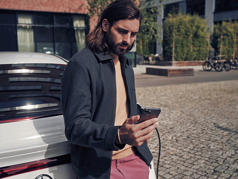 Man standing next to white Mercedes-Benz EQE holding phone