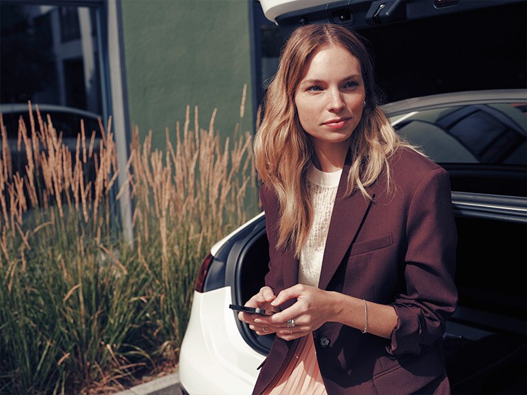 Woman sitting on white Mercedes-Benz car holding phone