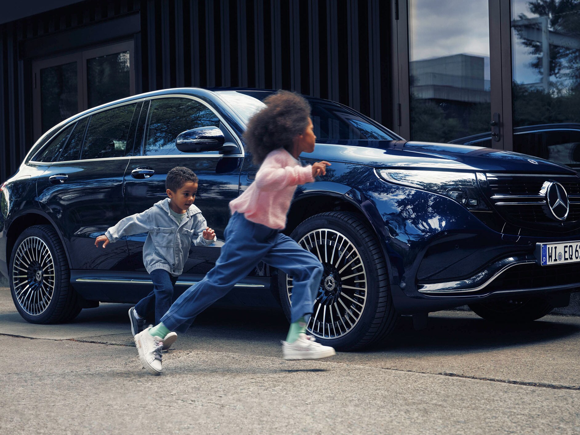 Children running next to blue Mercedes-Benz EQC