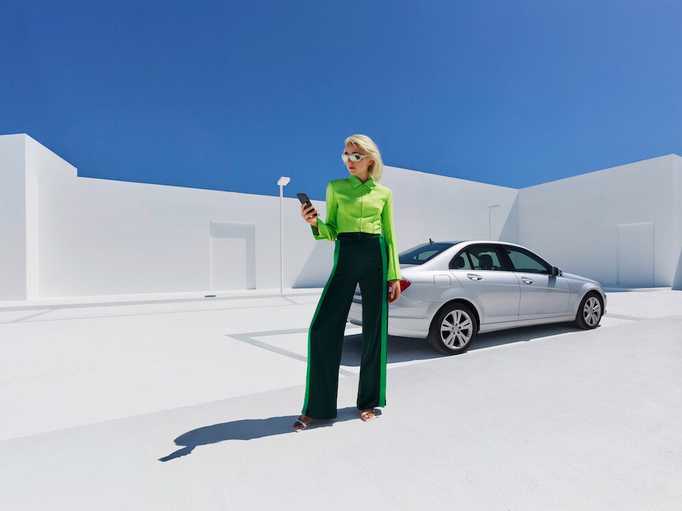 A woman standing in front of a Mercedes-Benz looking at her smartphone.