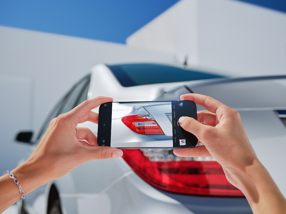 Someone photographing vehicle damage on a Mercedes-Benz using their smartphone.