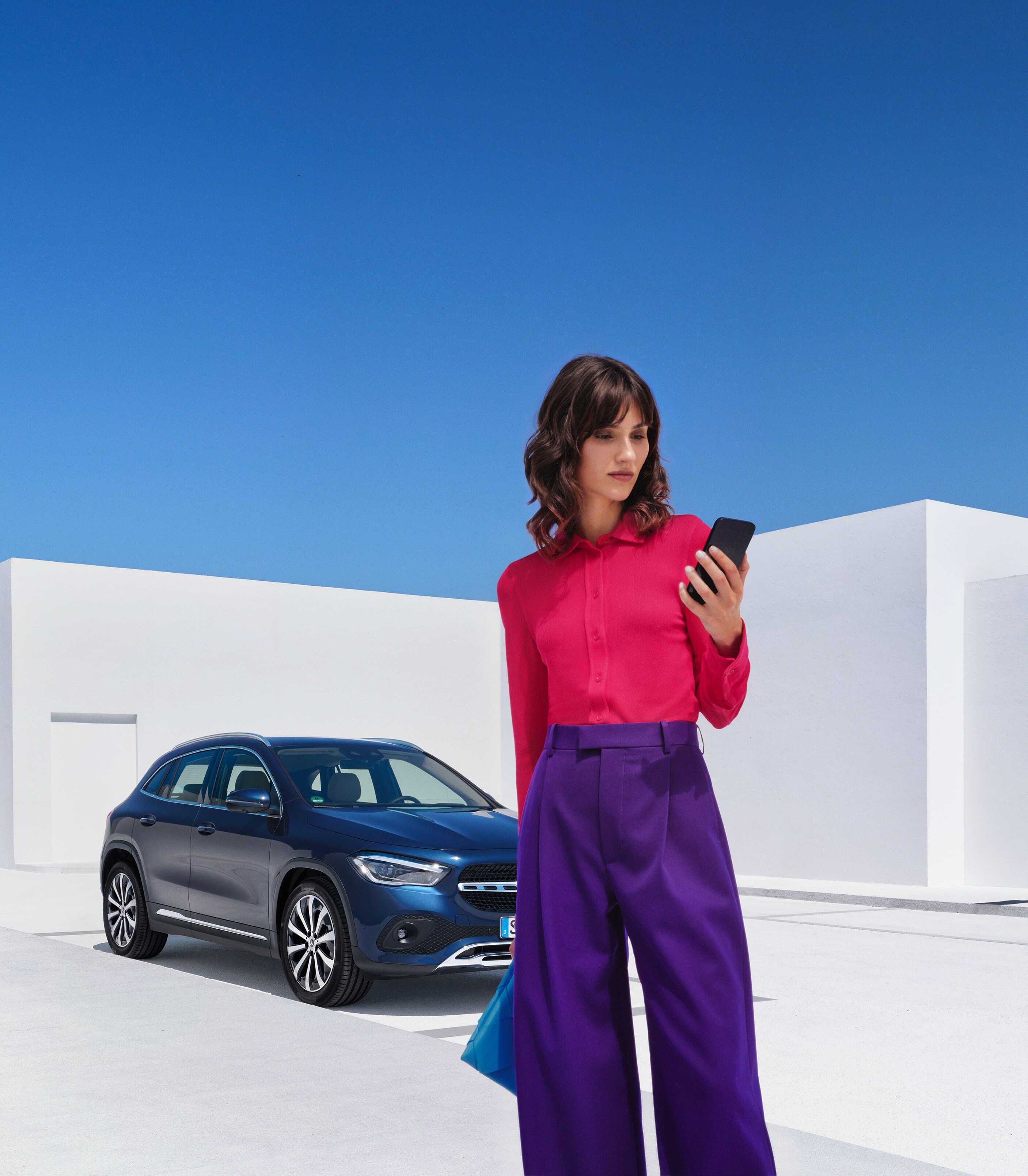 A woman standing in front of a Mercedes-Benz looking at her smartphone.