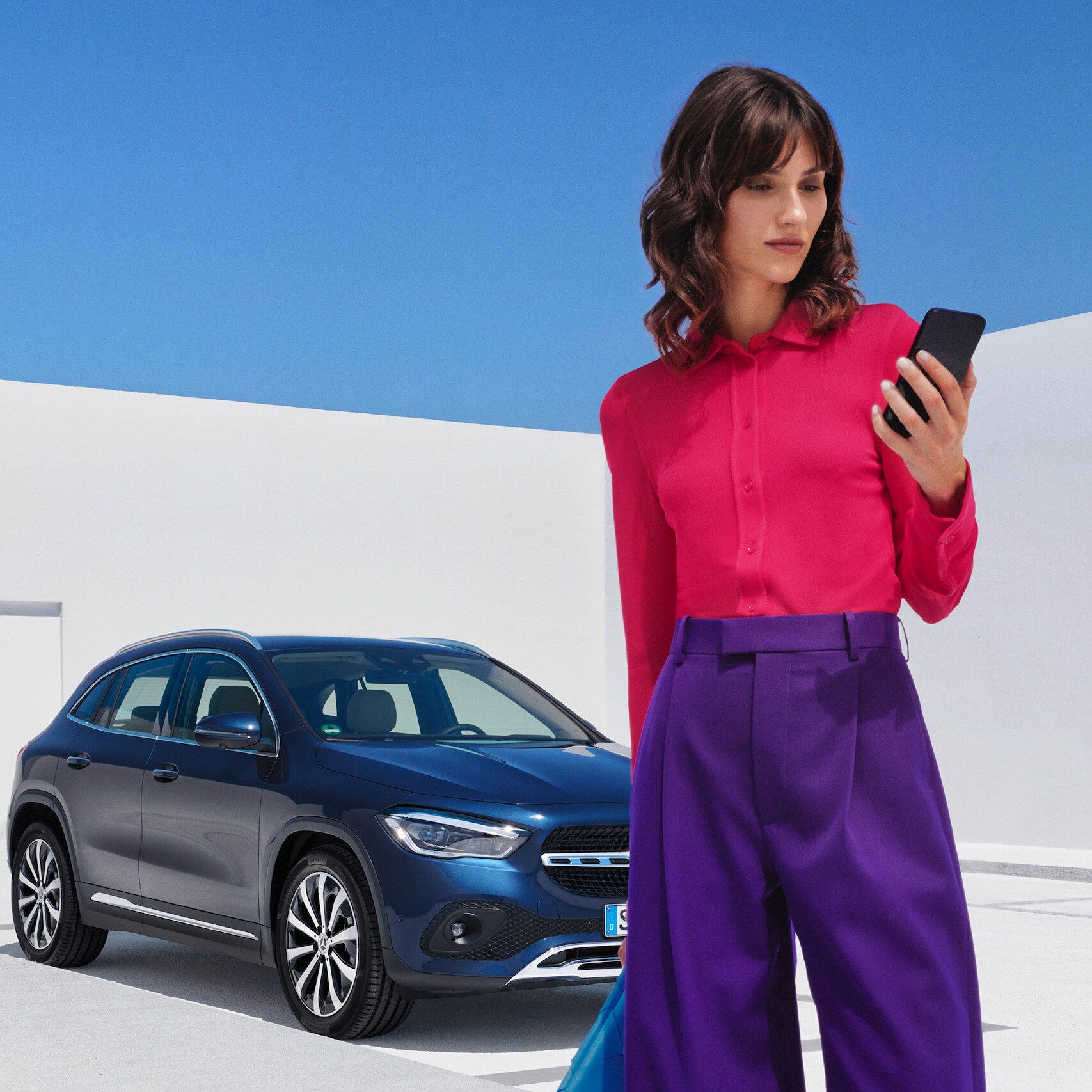 A woman in front of a Mercedes-Benz looking at her smartphone.