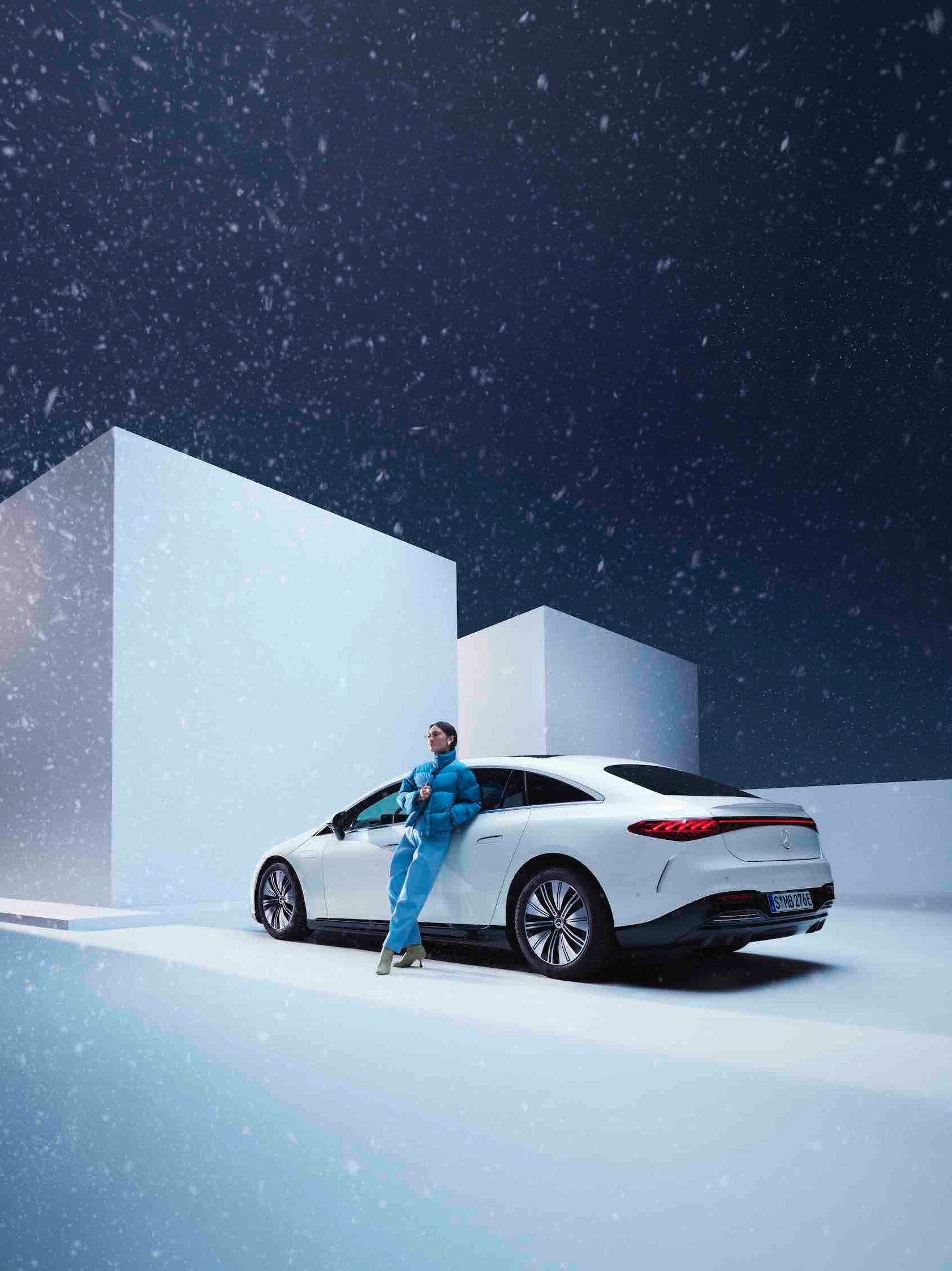 A woman leans on her Mercedes while it's snowing.