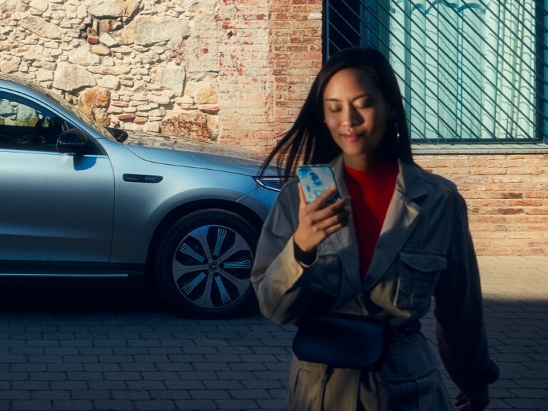 A woman uses the Mercedes-Benz App on her smartphone to connect to her Mercedes-Benz.