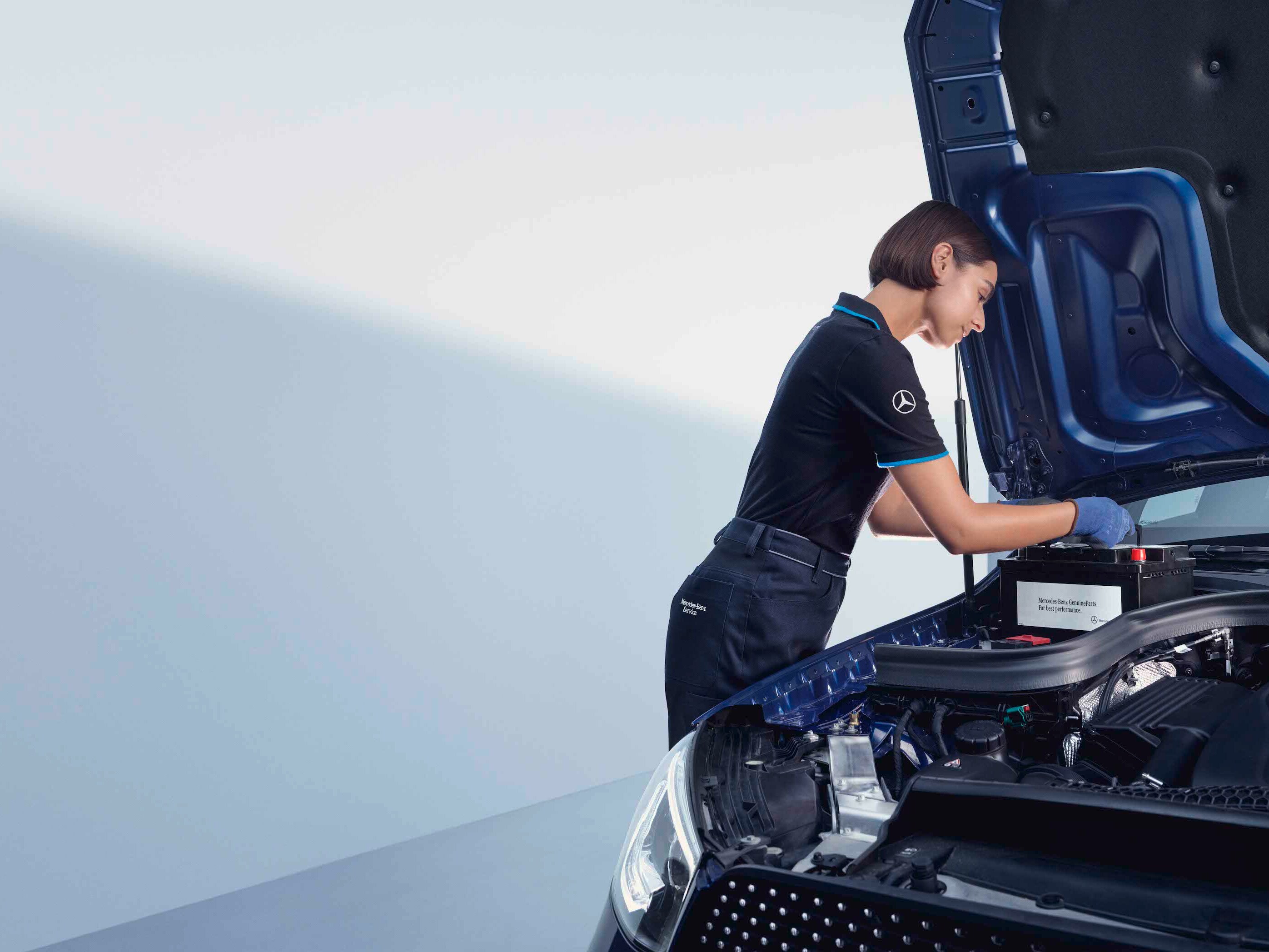A automotive mechanic bends over the open bonnet of a Mercedes-Benz.
