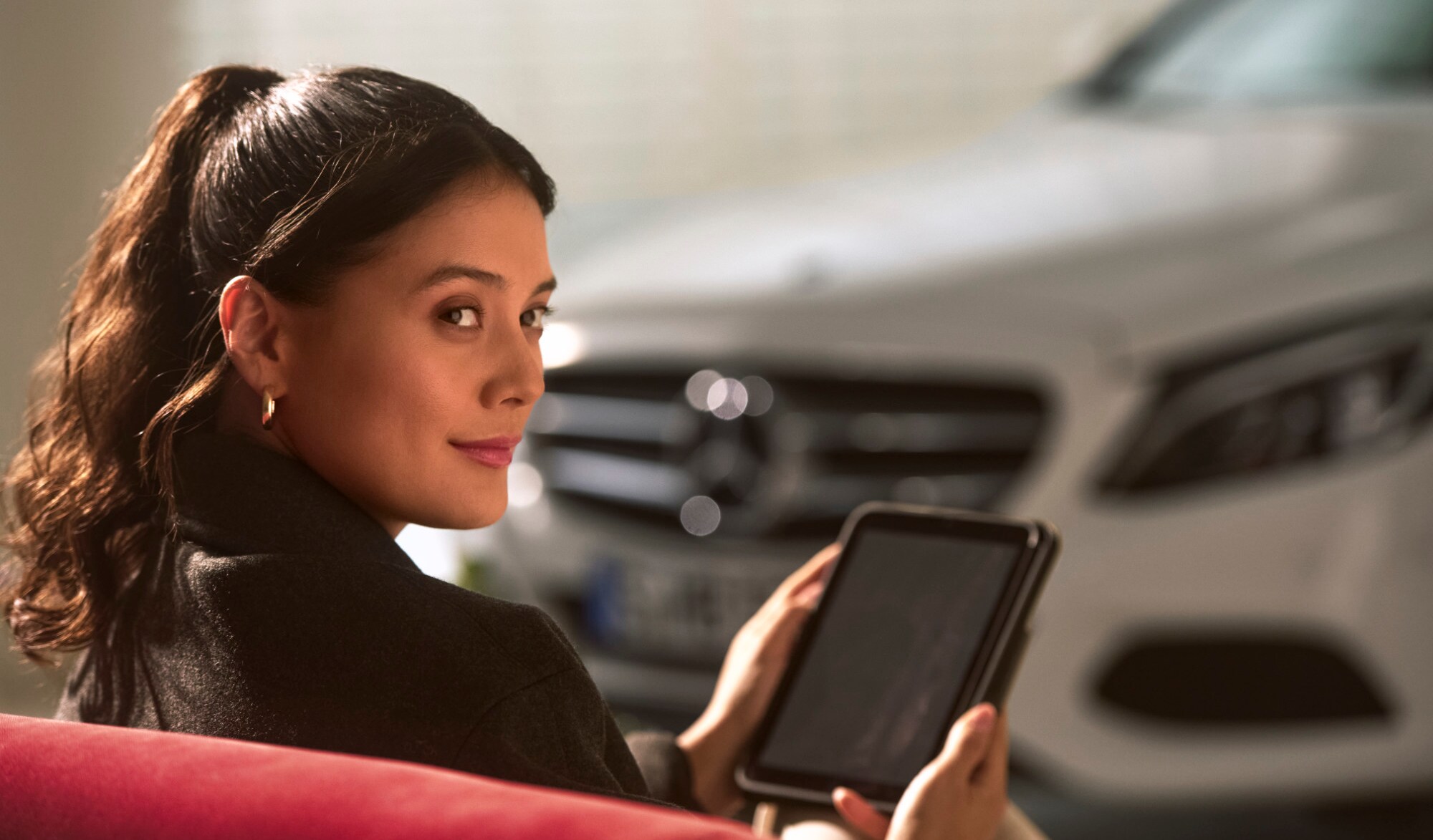 A person sitting next to a Mercedes-Benz vehicle with a tablet in their hands.