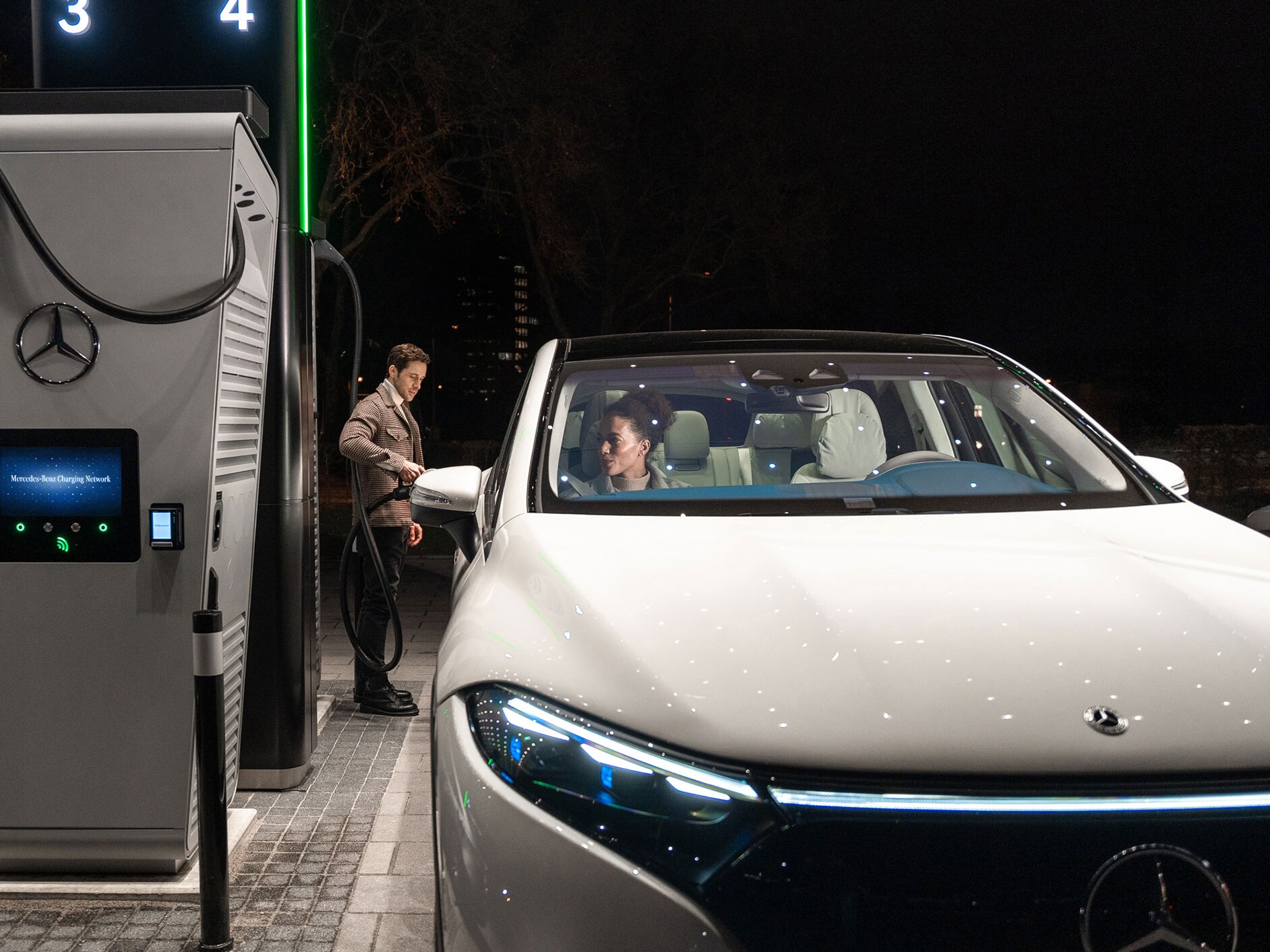 A person charging a Mercedes-Benz EQS SUV at a charging station.