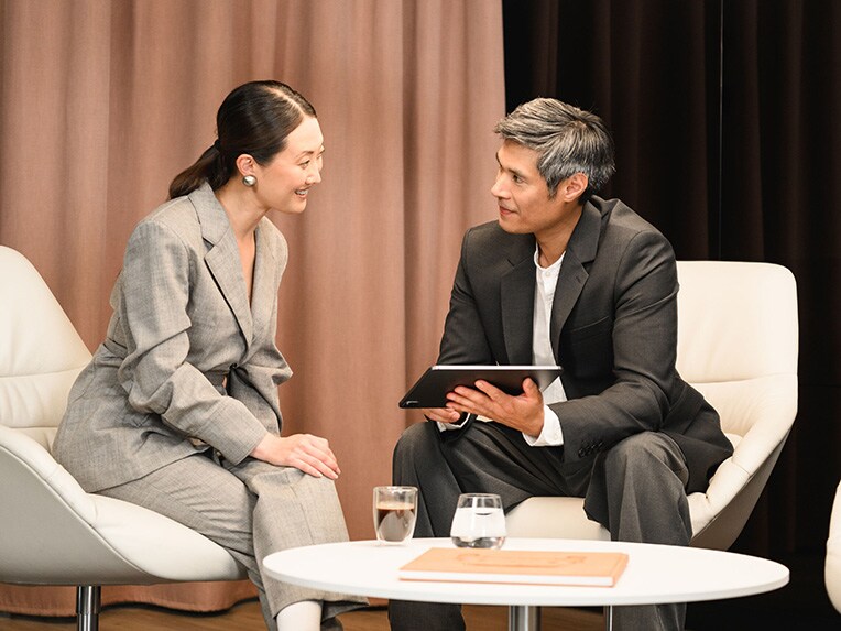 One person showing another person someting on a mobile device whilst seated.
