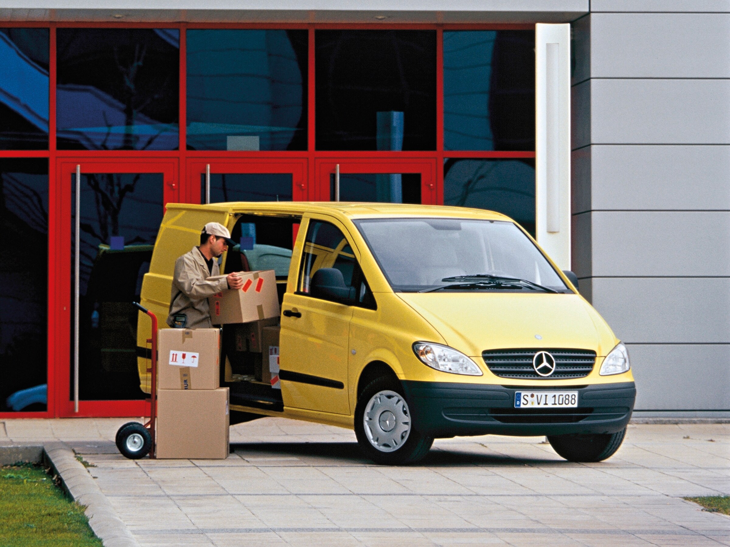 Yellow Mercedes-Benz Vito parked outside building with worker unloading packages