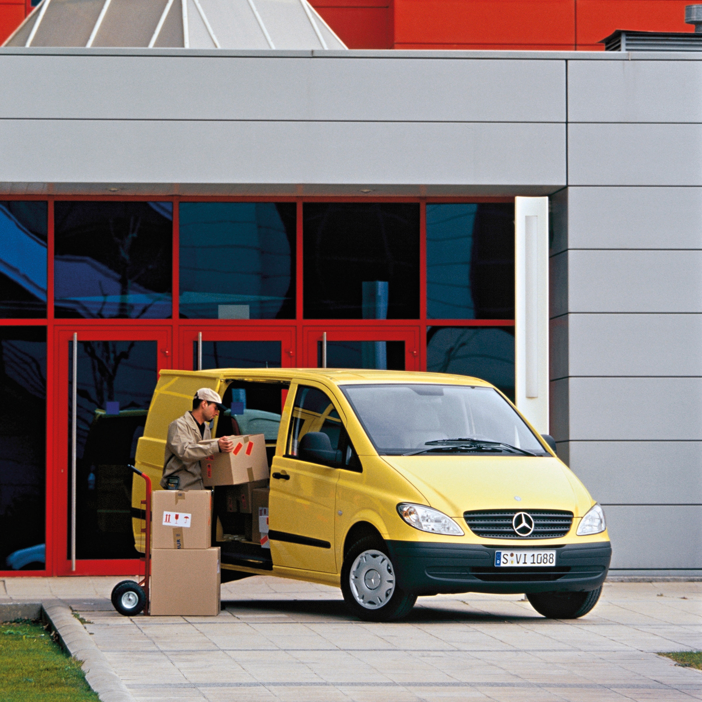 The second generation of Mercedes-Benz Vitos | Commercial Vehicles History | Mercedes-Benz Yellow Mercedes-Benz Vito parked outside building with worker unloading packages