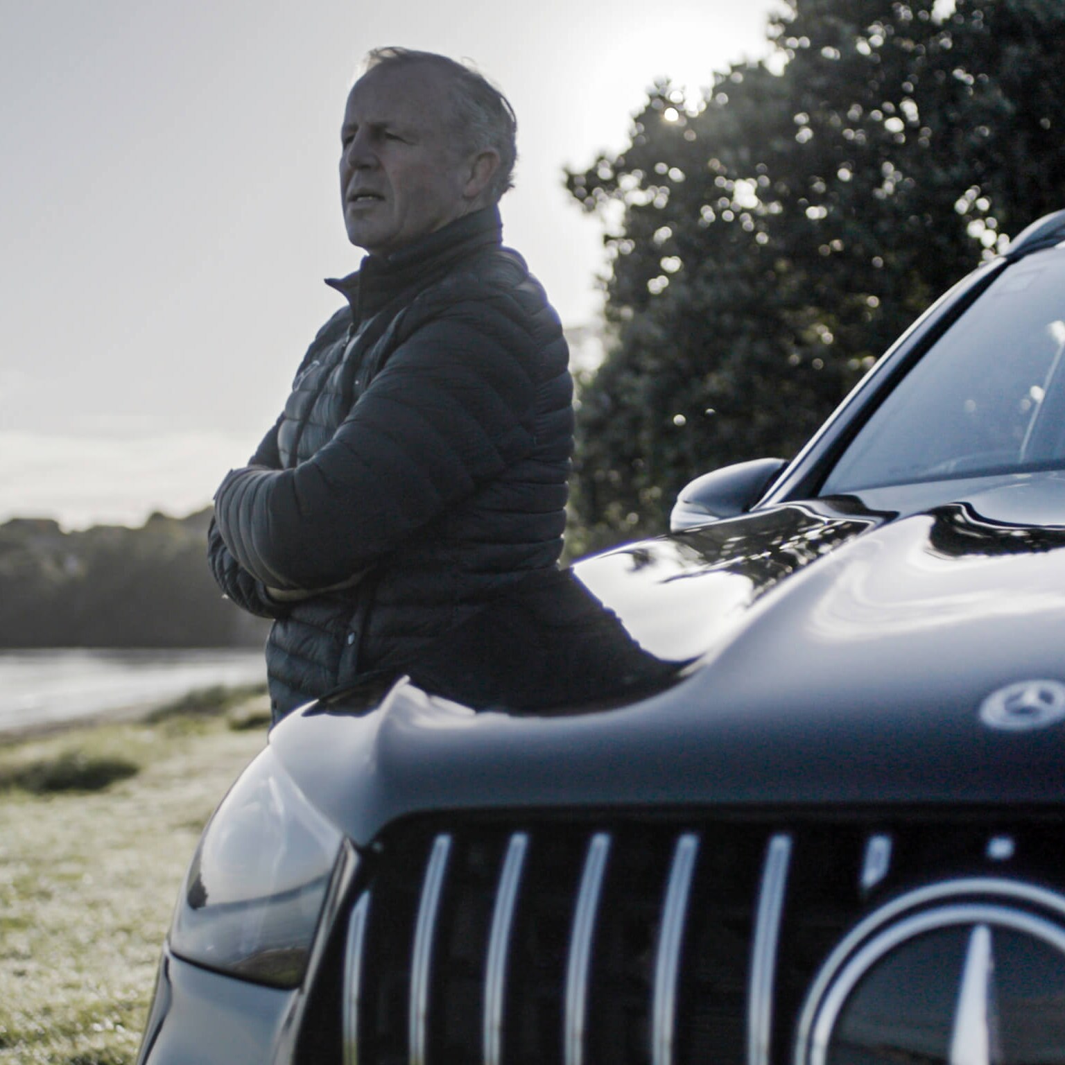 Sean Fitzpatrick stands next to black Mercedes-Benz vehicle overlooking the water.